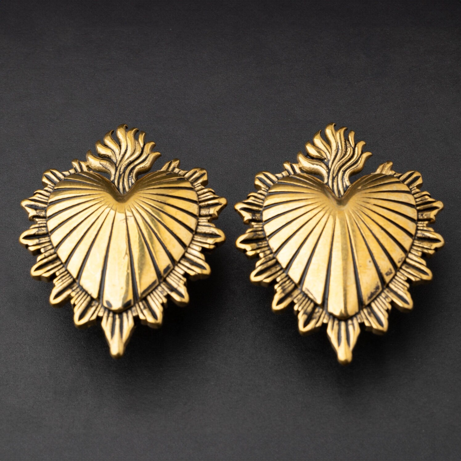 Sacred Heart-inspired plugs in gold, displayed on a matte dark background, showcasing intricate detailing and a bold design.