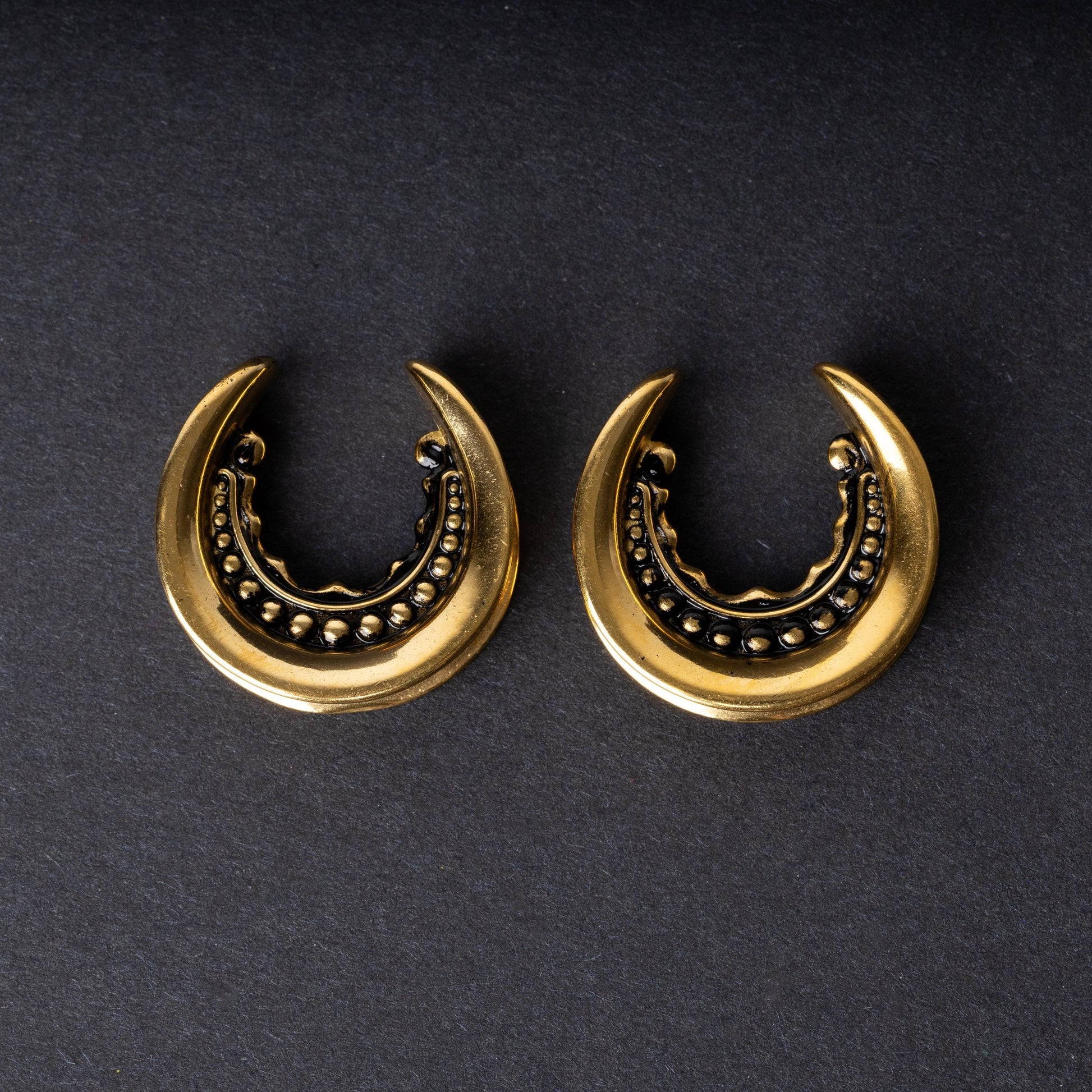 Gold crescent-shaped earrings with detailed accents, displayed on a dark background.