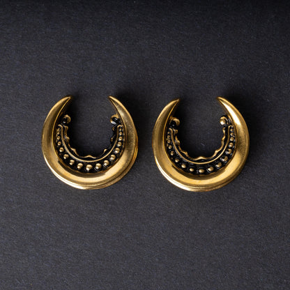 Gold crescent-shaped earrings with detailed accents, displayed on a dark background.