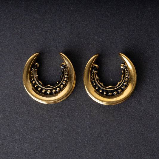 Gold crescent-shaped earrings with detailed accents, displayed on a dark background.