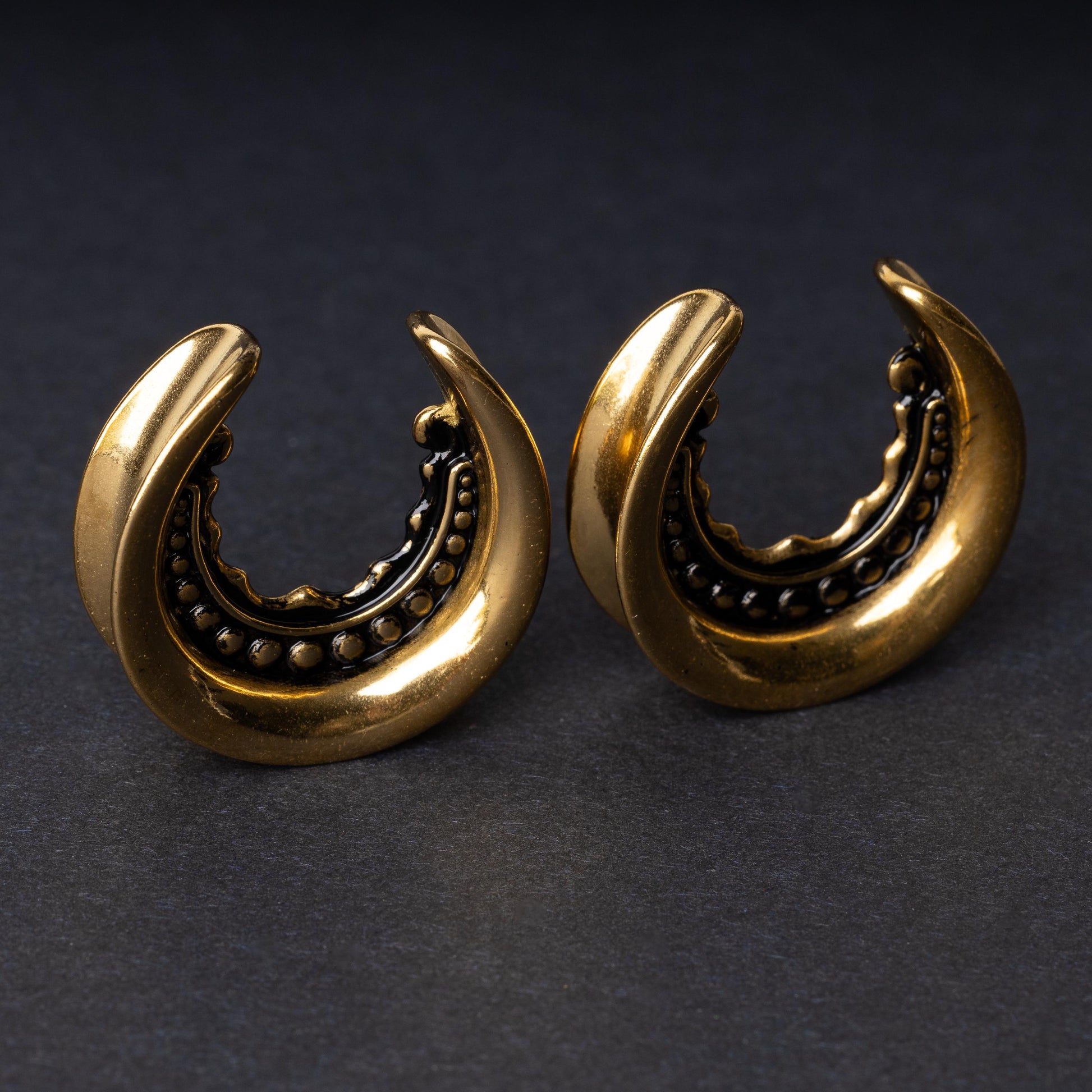 Gold crescent-shaped earrings with detailed accents, displayed on a dark background.