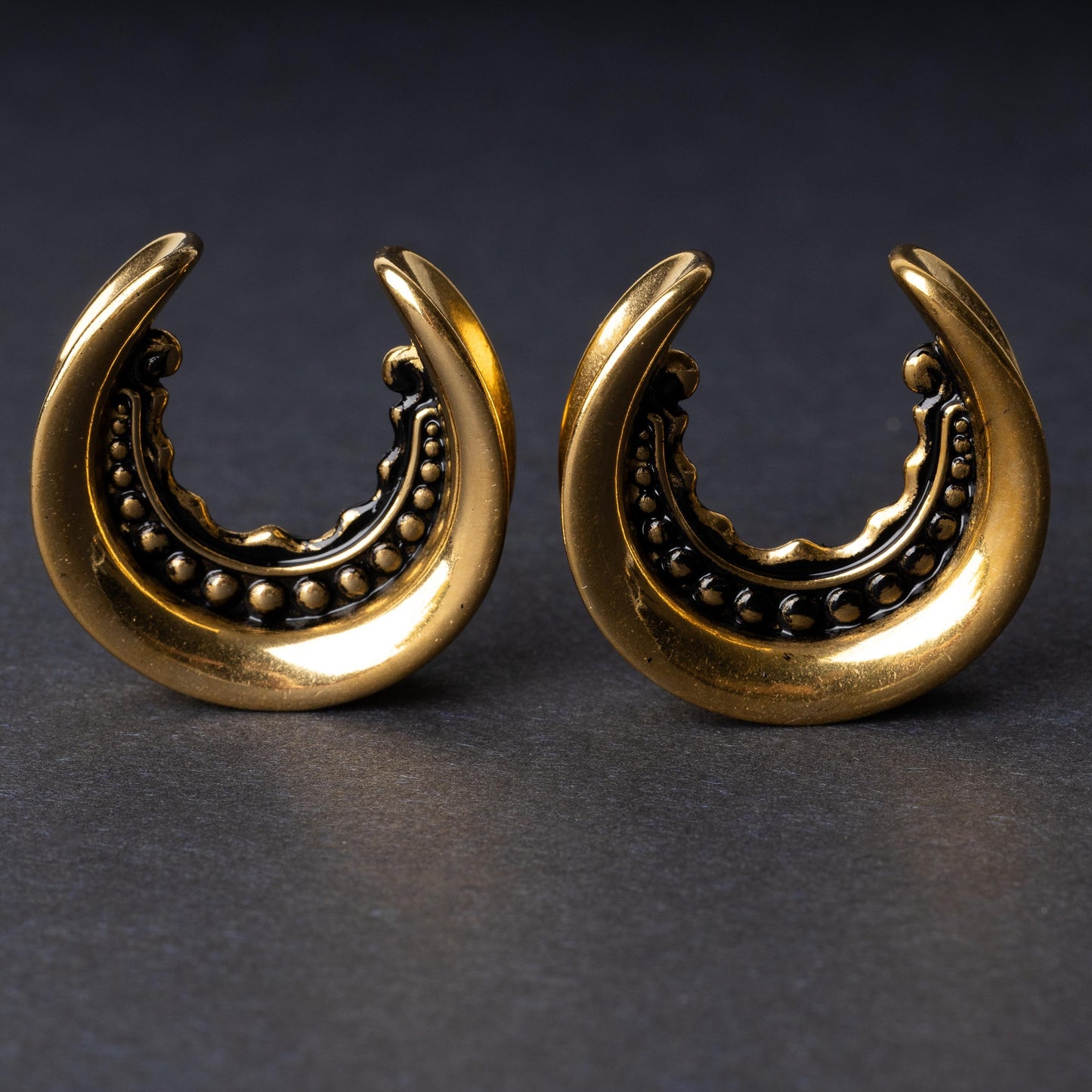 Gold crescent-shaped earrings with detailed accents, displayed on a dark background
