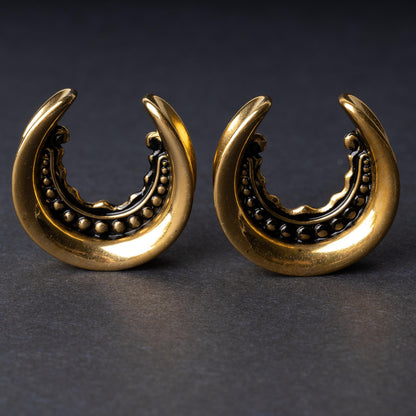 Gold crescent-shaped earrings with detailed accents, displayed on a dark background