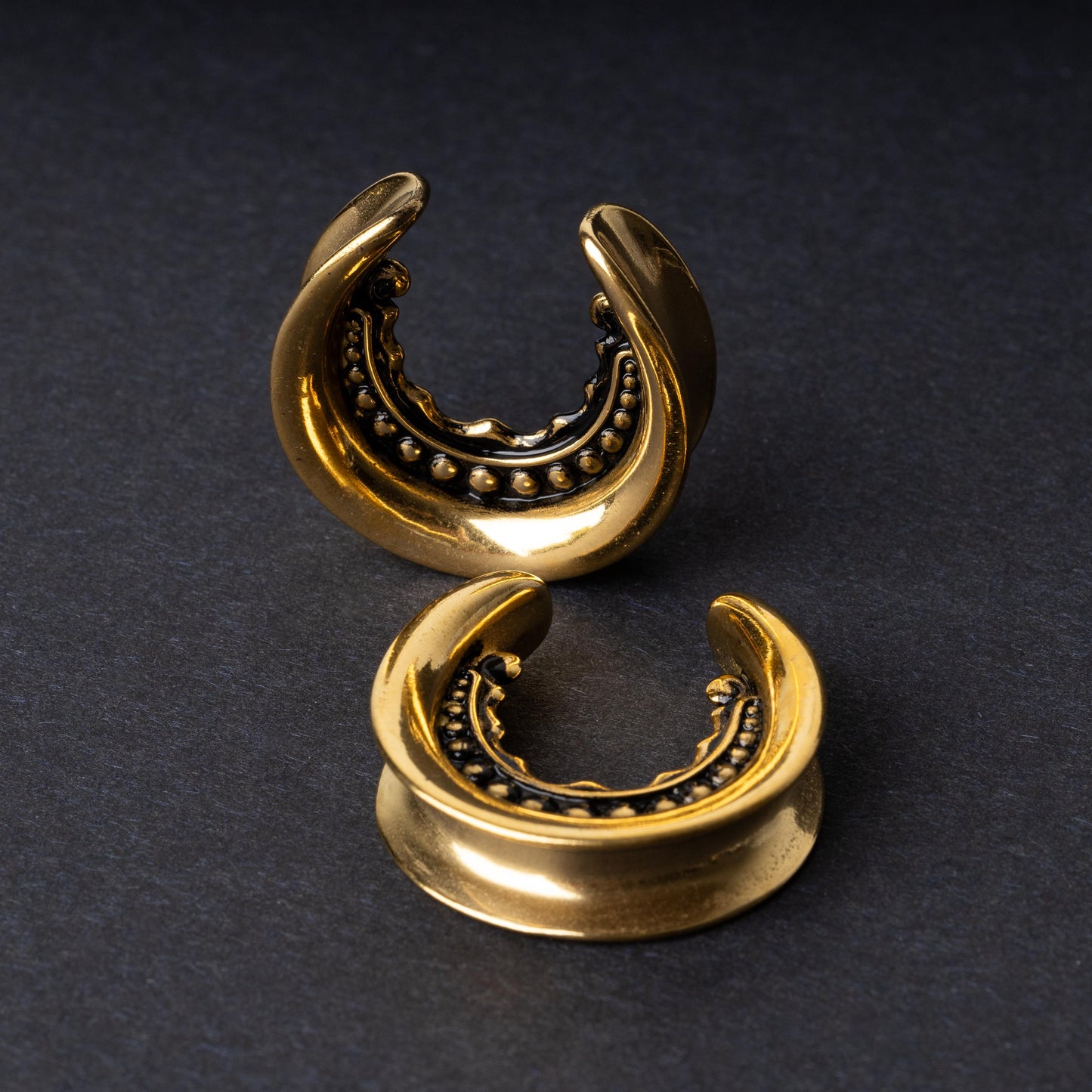 Gold crescent-shaped earrings with detailed accents, displayed on a dark background