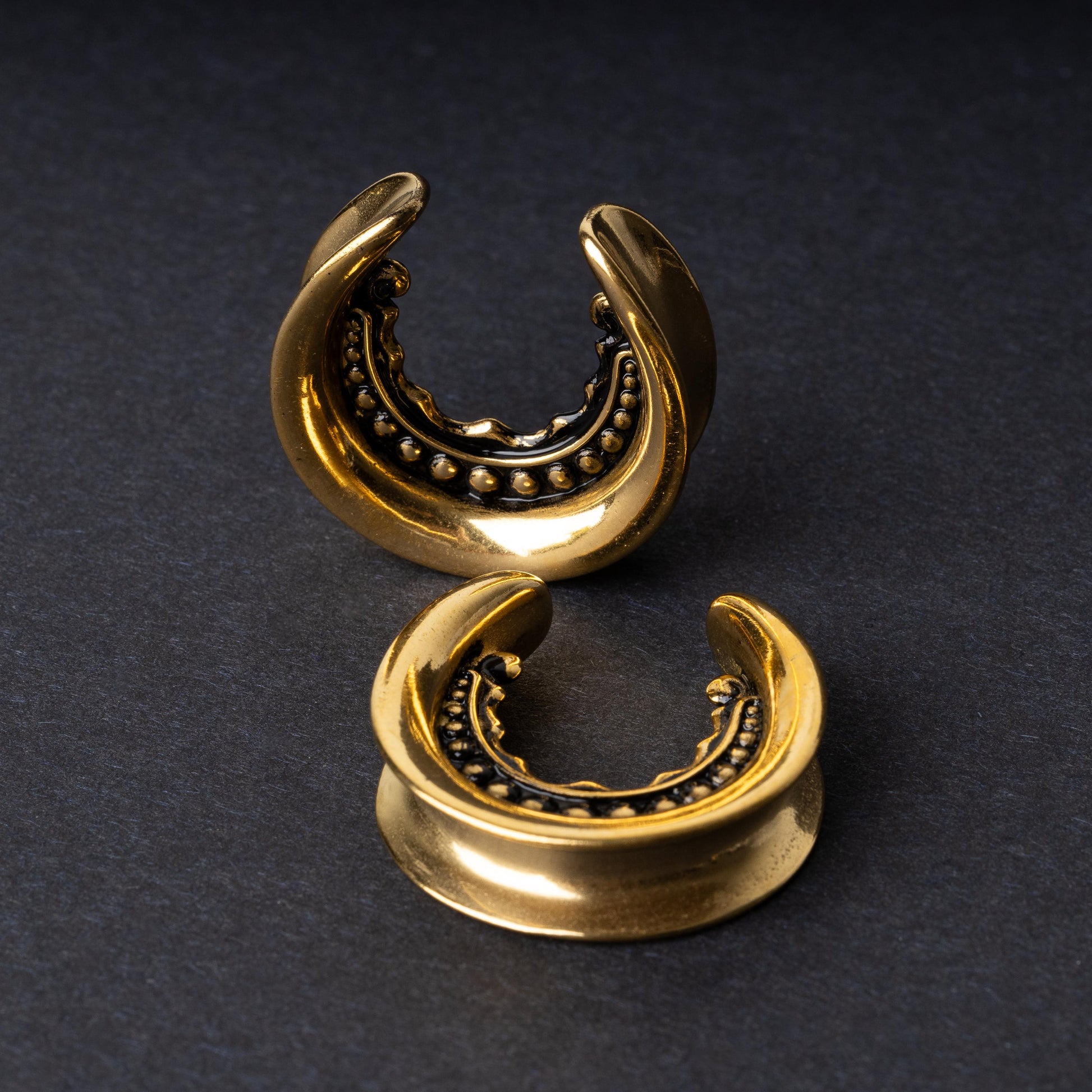 Gold crescent-shaped earrings with detailed accents, displayed on a dark background