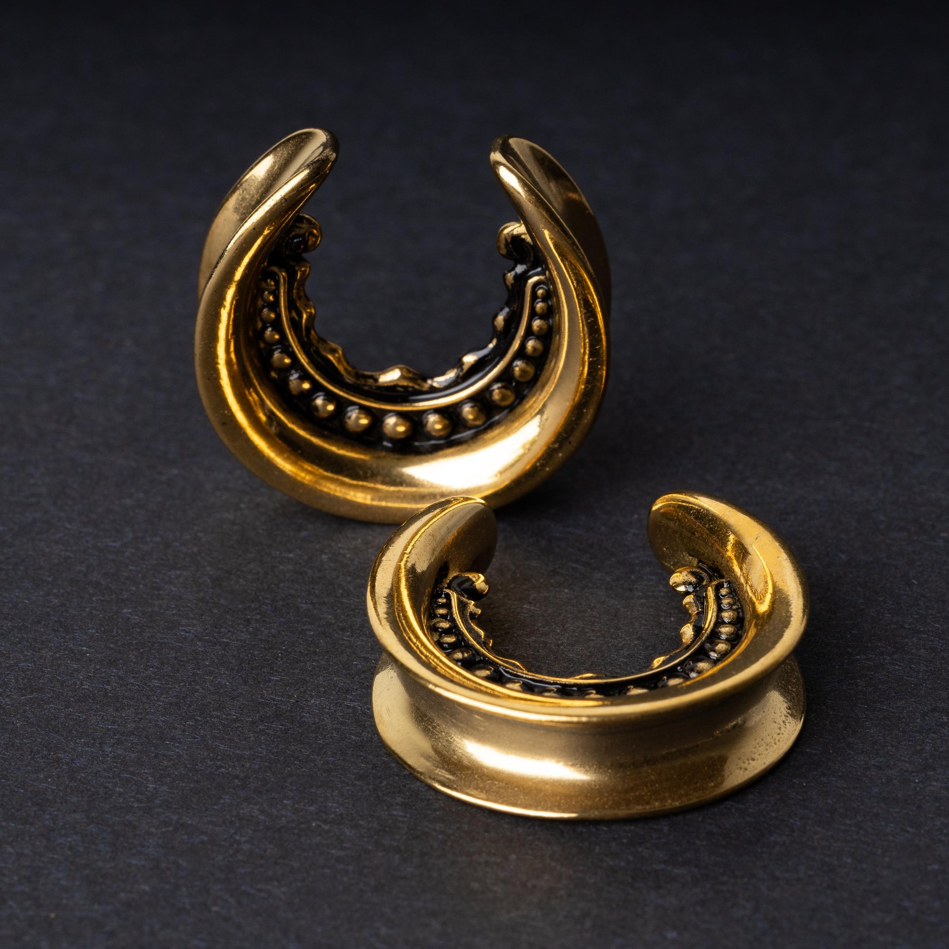 Gold crescent-shaped earrings with detailed accents, displayed on a dark background.