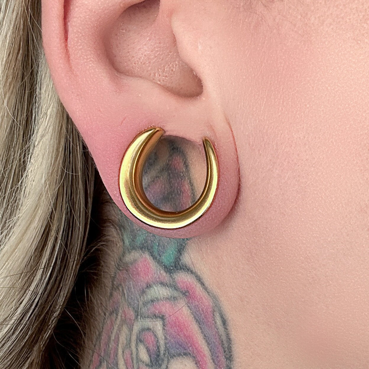 A single Gold Saddle Tunnels displayed in a models ear.