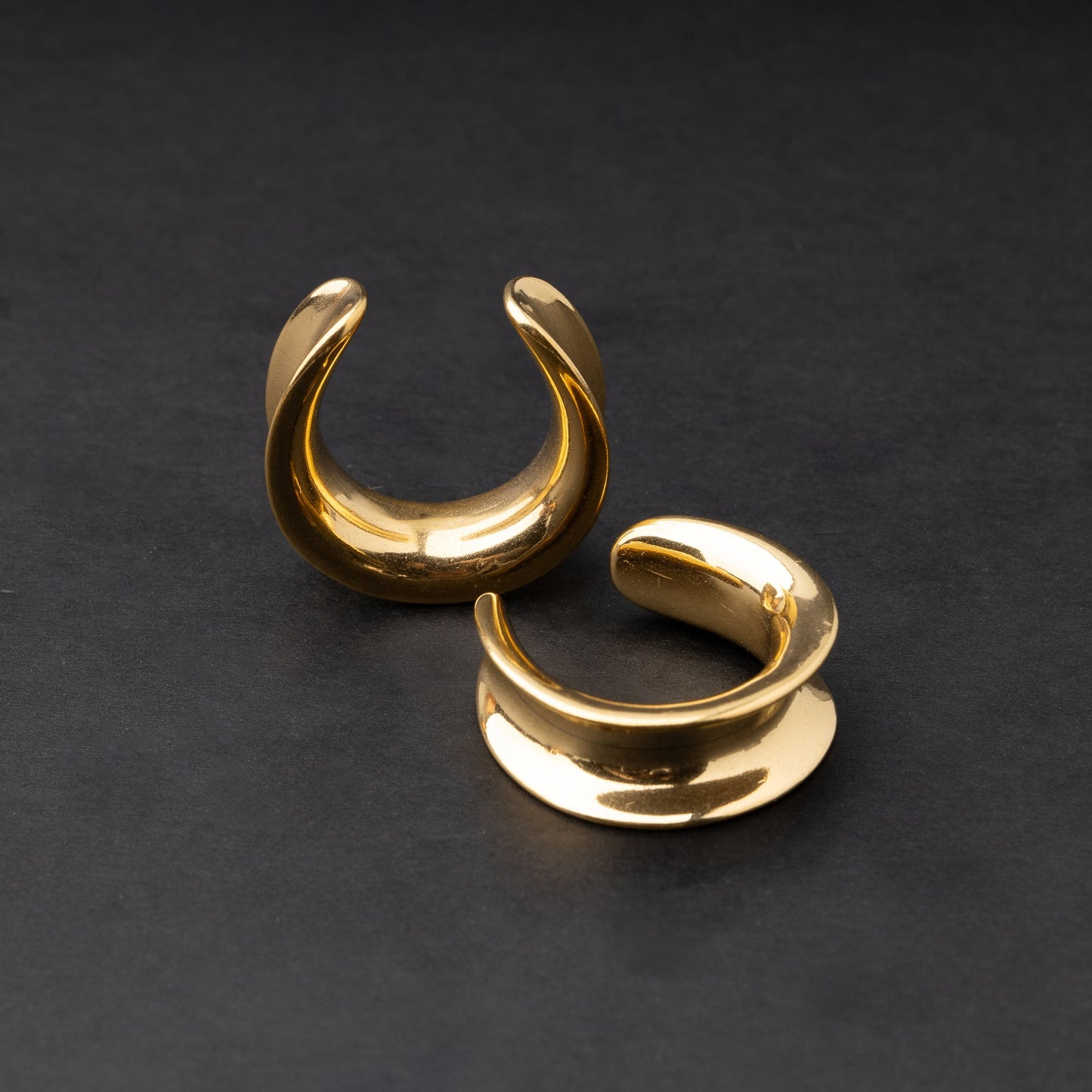 A pair of gold saddle tunnels displayed on a dark background.