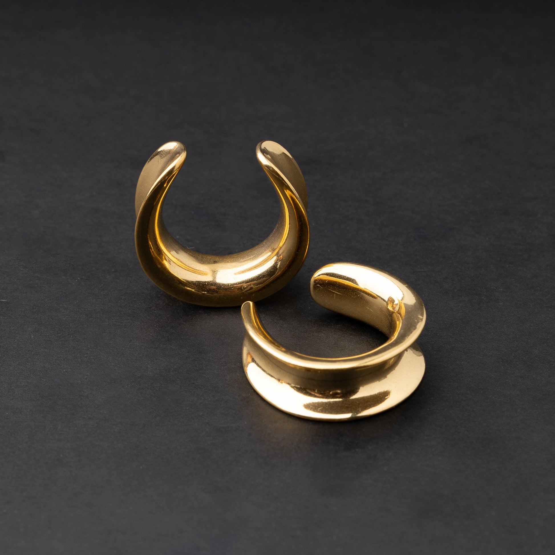 A pair of gold saddle tunnels displayed on a dark background.