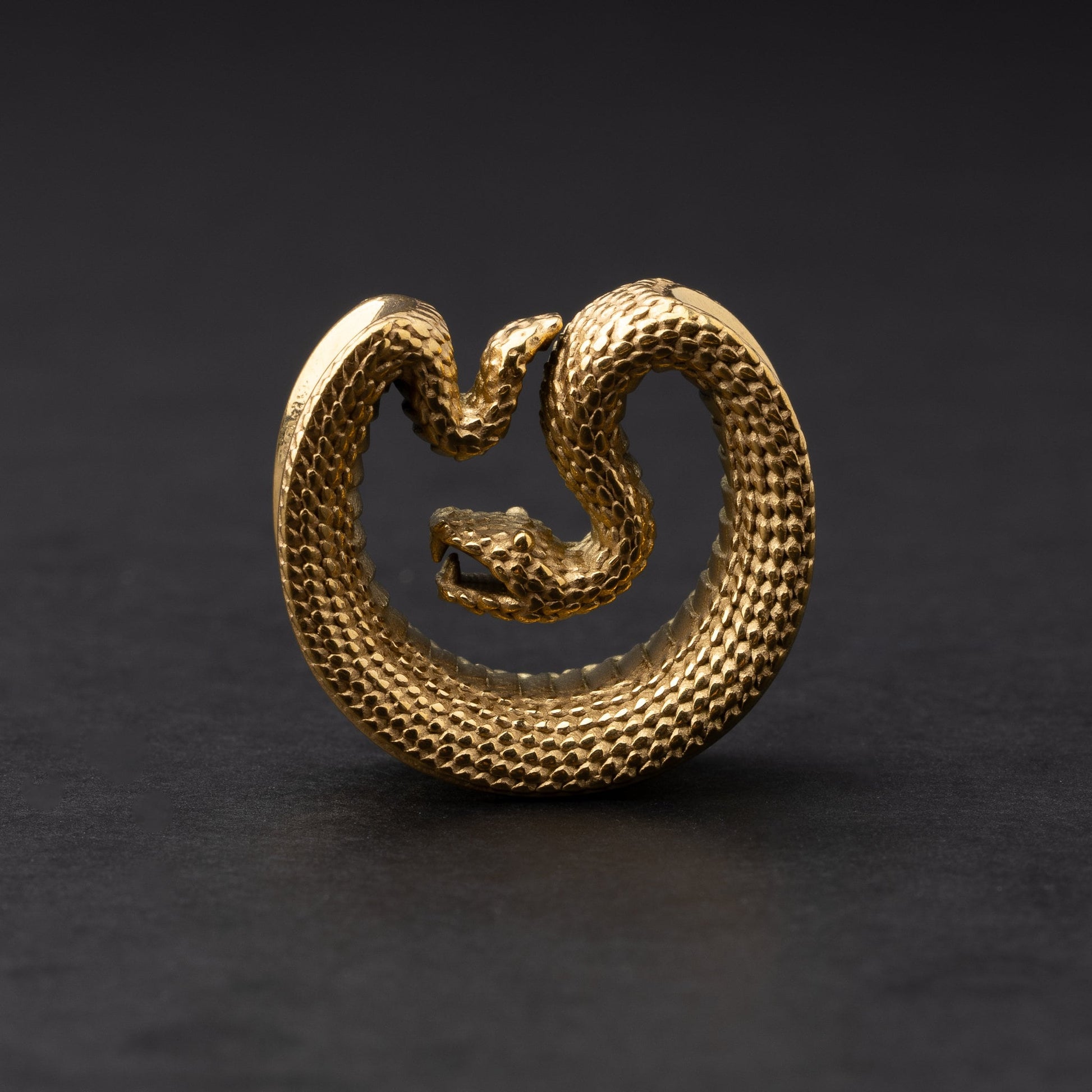Gold Snake-shaped saddle plugs, displayed on a dark background.