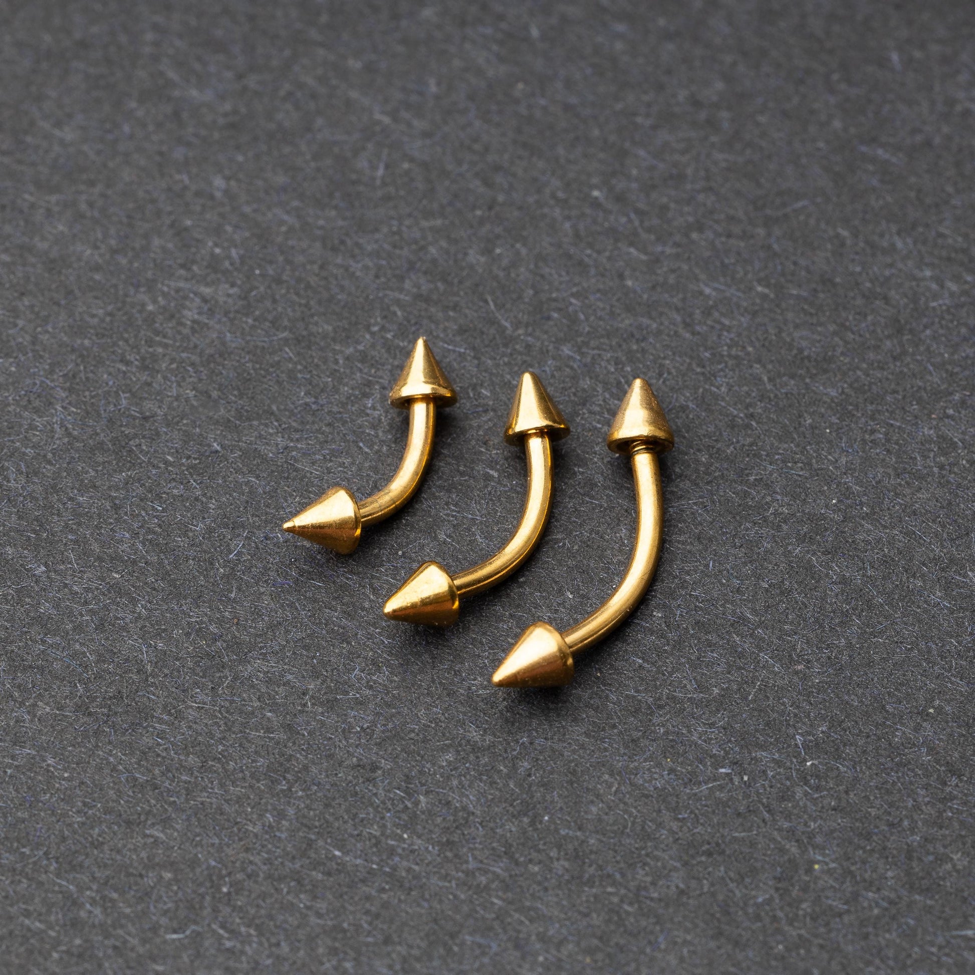 Gold curved barbells with pointed spike ends, displayed on a dark background.