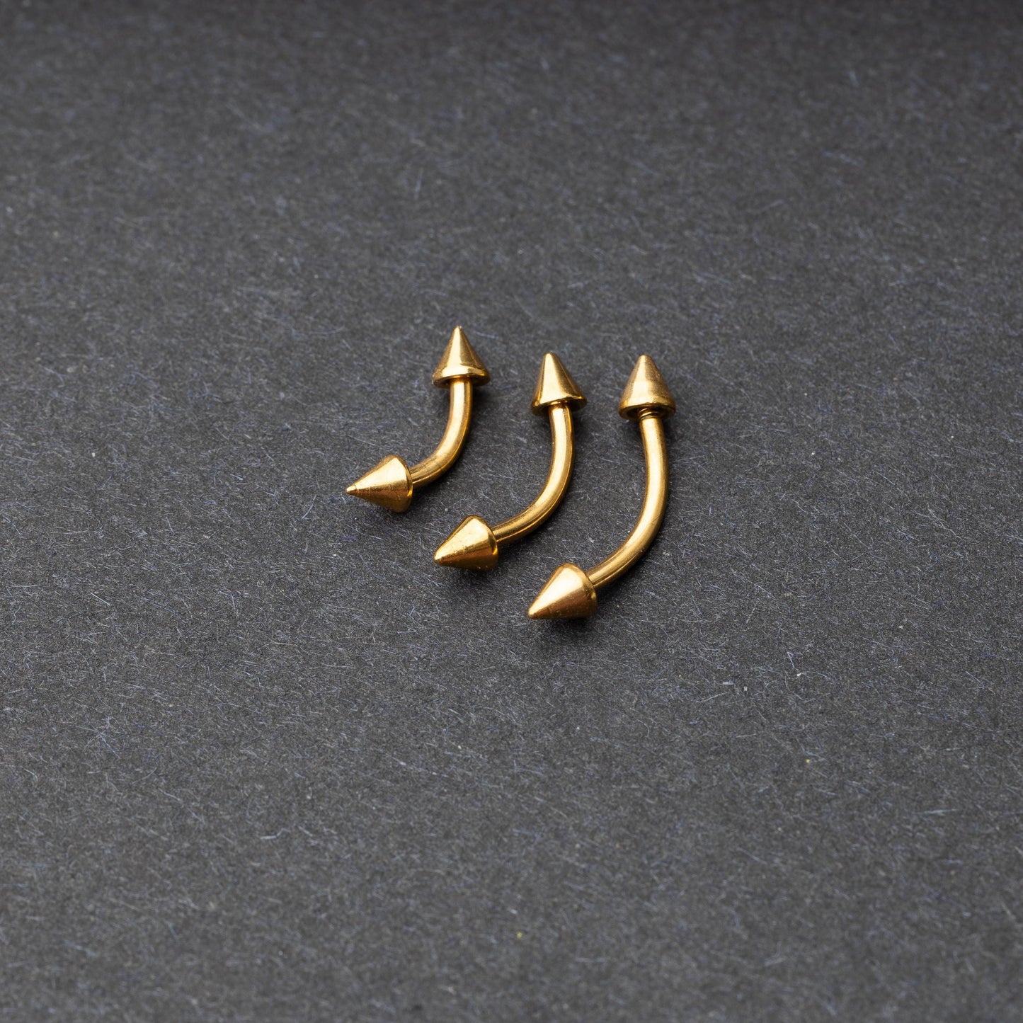 Gold curved barbells with pointed spike ends, displayed on a dark background.