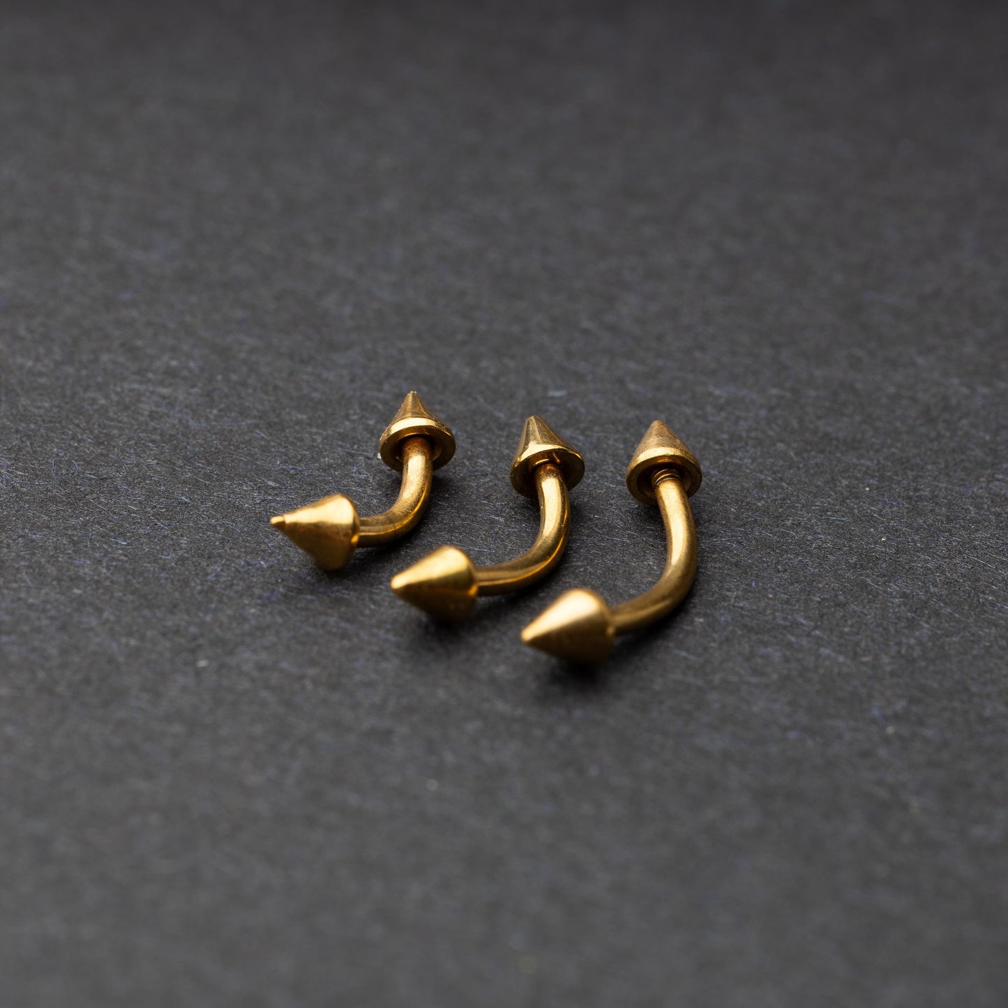 Gold curved barbells with pointed spike ends, displayed on a dark background.