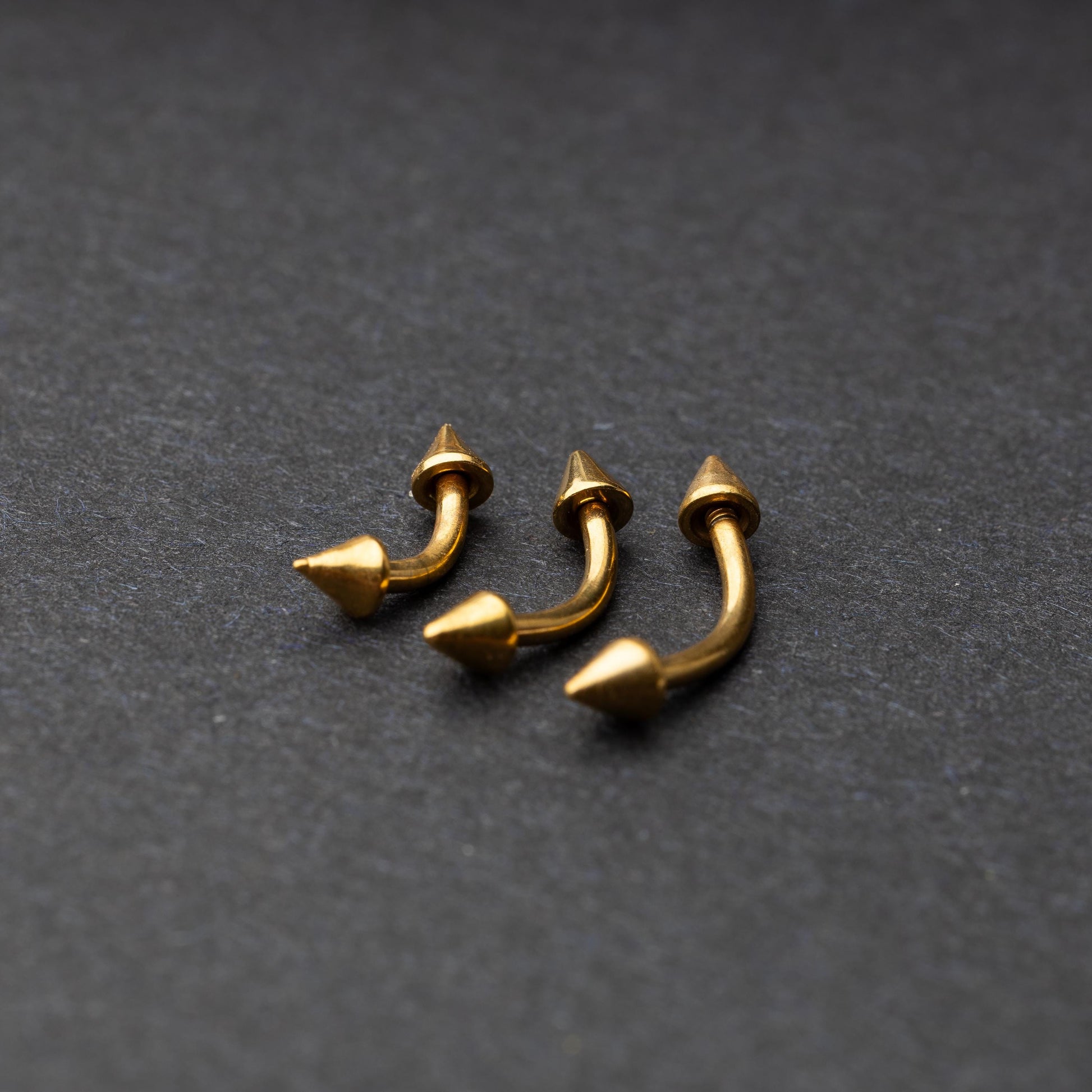 Gold curved barbells with pointed spike ends, displayed on a dark background.