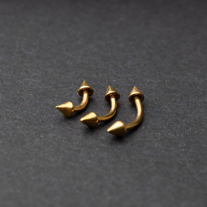 Gold curved barbells with pointed spike ends, displayed on a dark background.