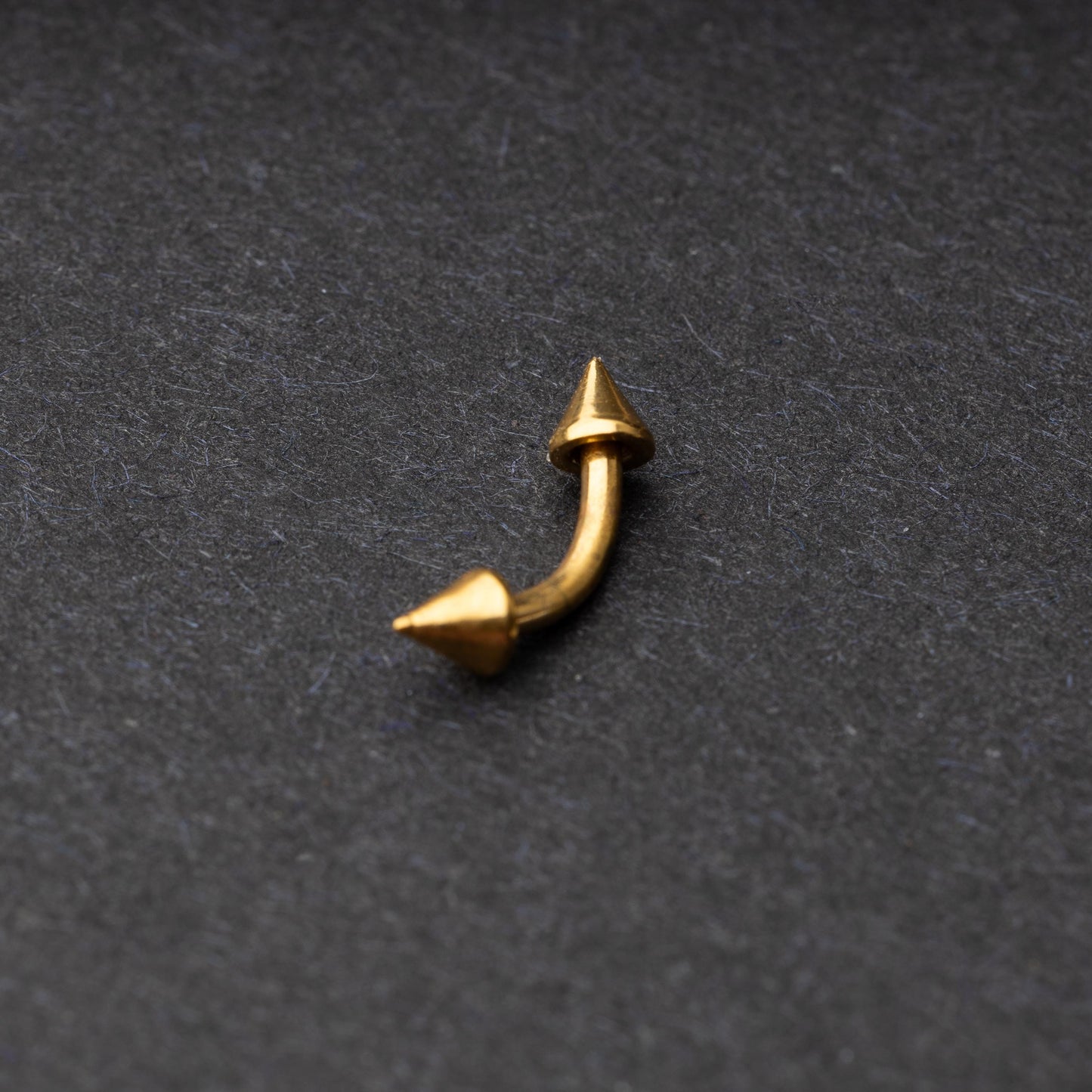 Gold curved barbell with pointed spike ends, displayed on a dark background.