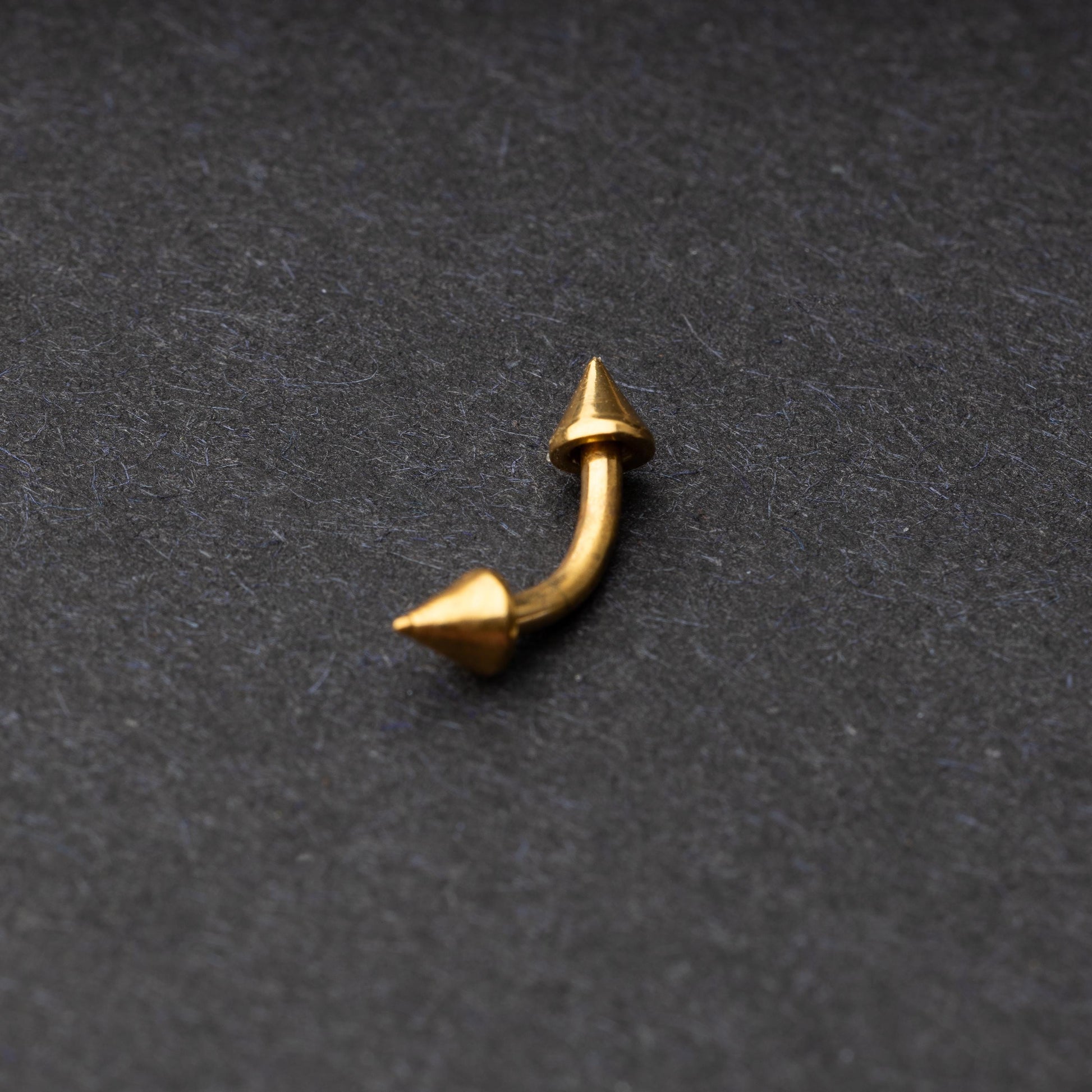 Gold curved barbell with pointed spike ends, displayed on a dark background.