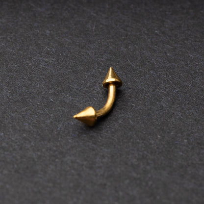 Gold curved barbell with pointed spike ends, displayed on a dark background.