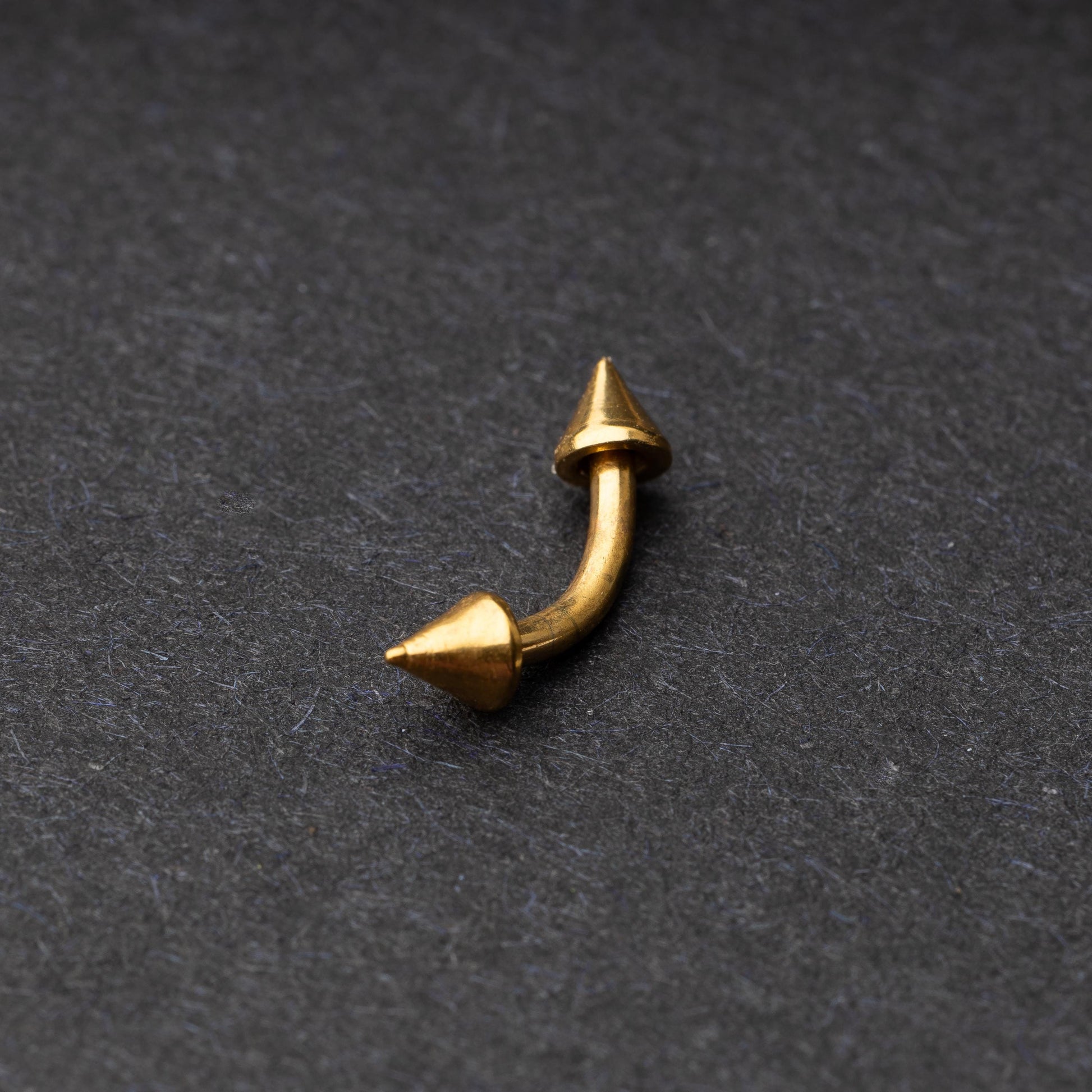Gold curved barbell with pointed spike ends, displayed on a dark background.