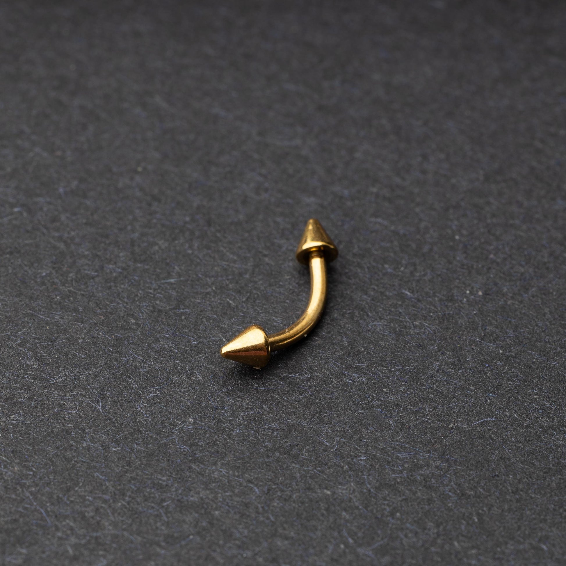 Gold curved barbell with pointed spike ends, displayed on a dark background.