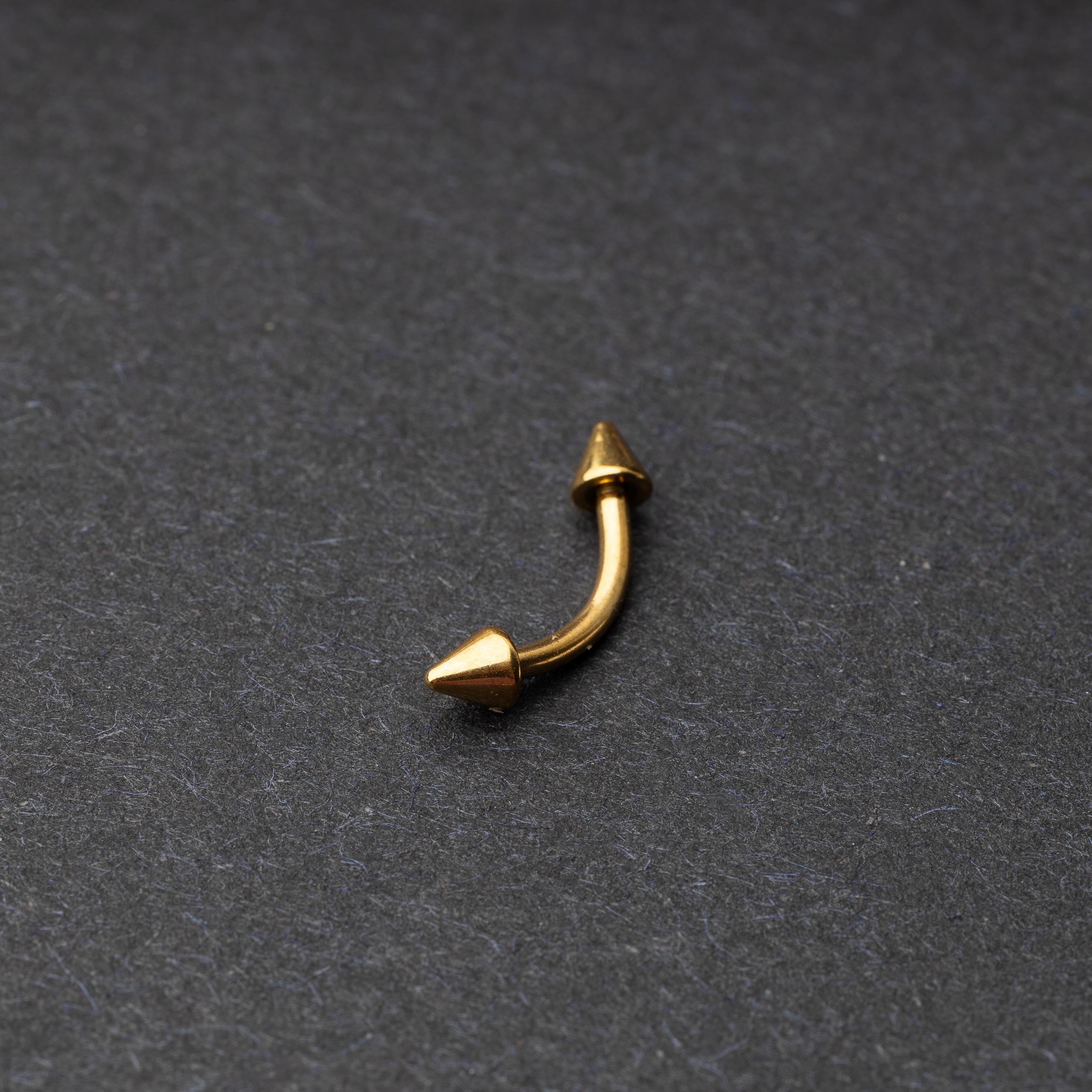 Gold curved barbell with pointed spike ends, displayed on a dark background.
