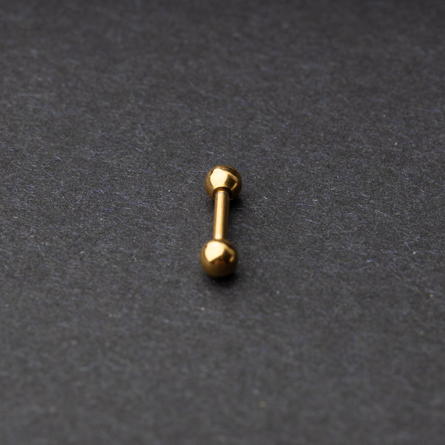 Gold-tone stainless steel barbell with polished spheres on a dark background.