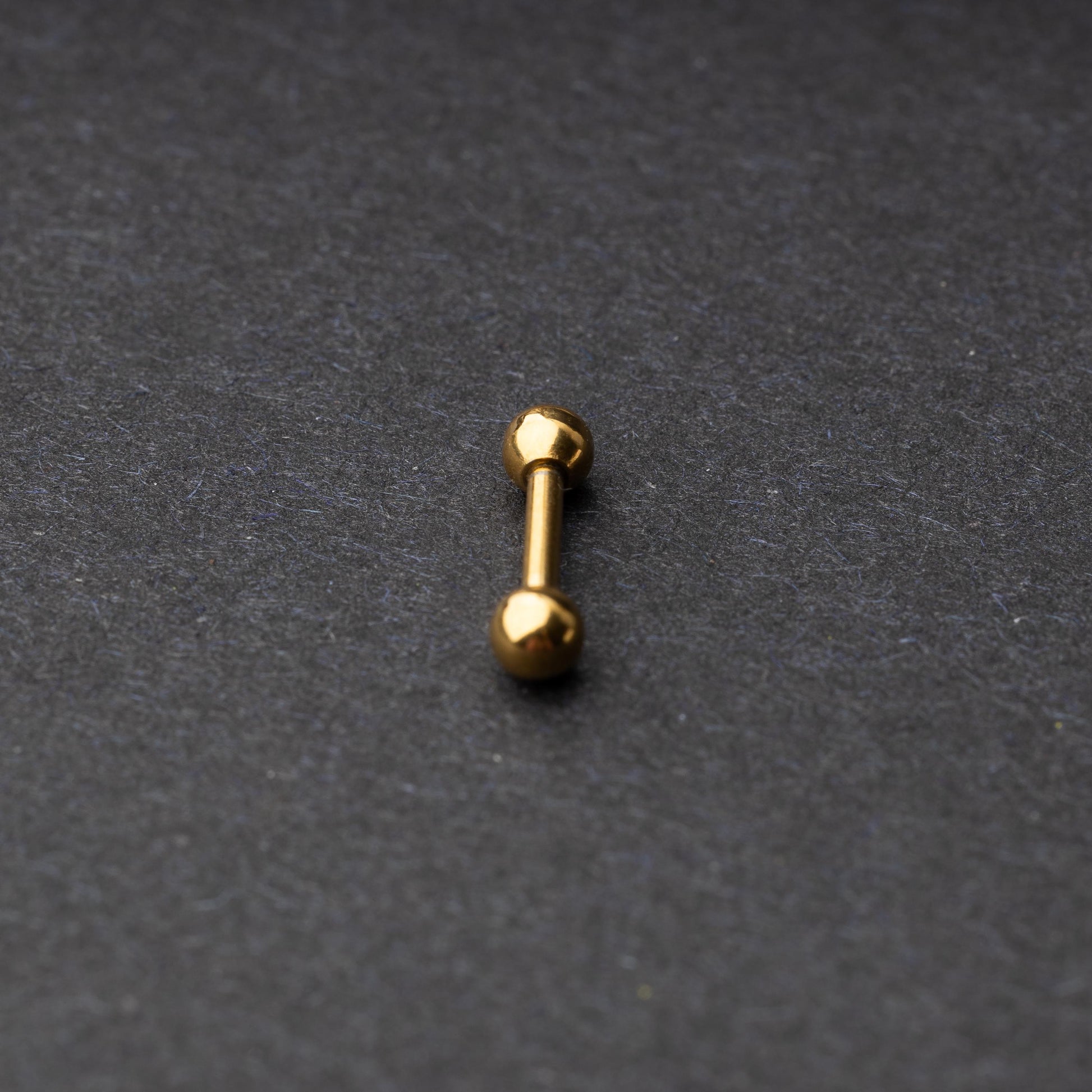 Gold-tone stainless steel barbell with polished spheres on a dark background.