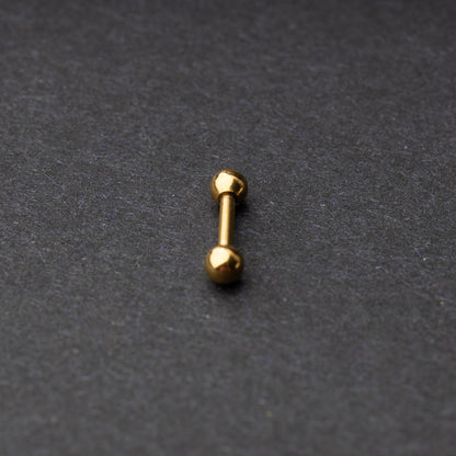 Gold-tone stainless steel barbell with polished spheres on a dark background.