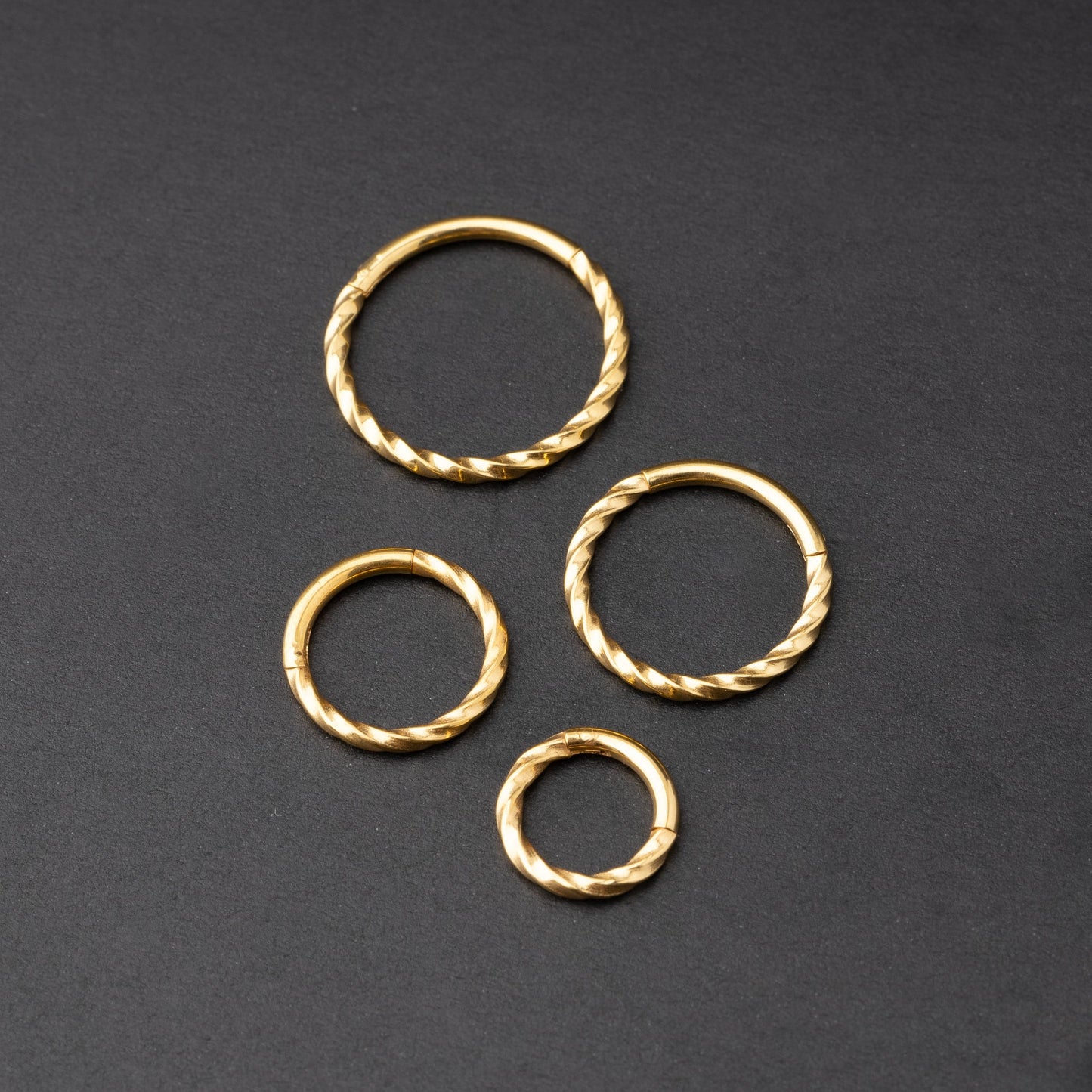 Gold twisted clicker rings in varying sizes, displayed on a dark background.