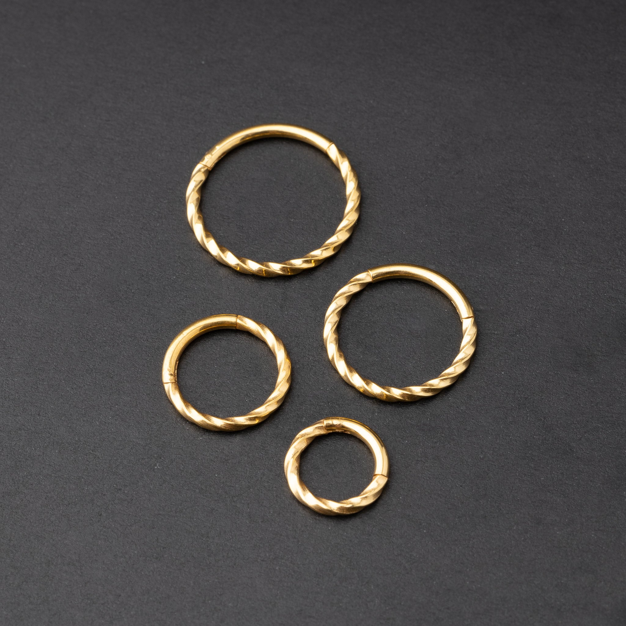 Gold twisted clicker rings in varying sizes, displayed on a dark background.