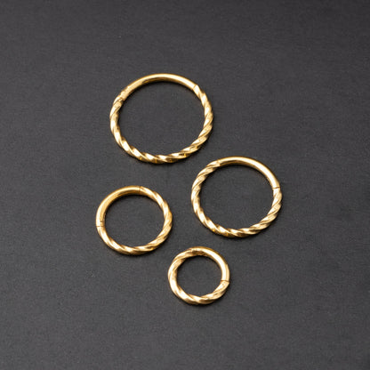 Gold twisted clicker rings in varying sizes, displayed on a dark background.