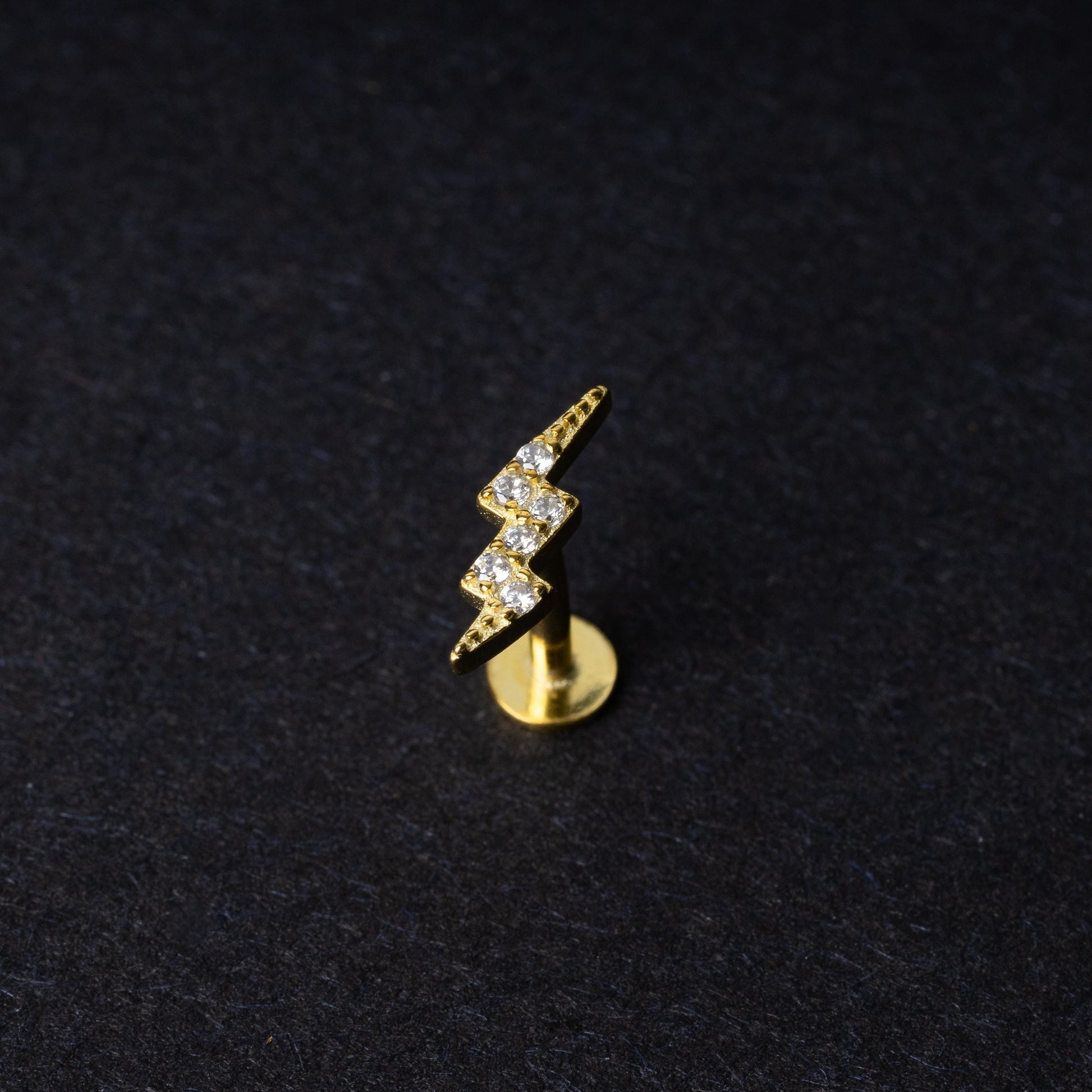 Gold lightning bolt labret stud with crystal detailing, displayed on a dark background.