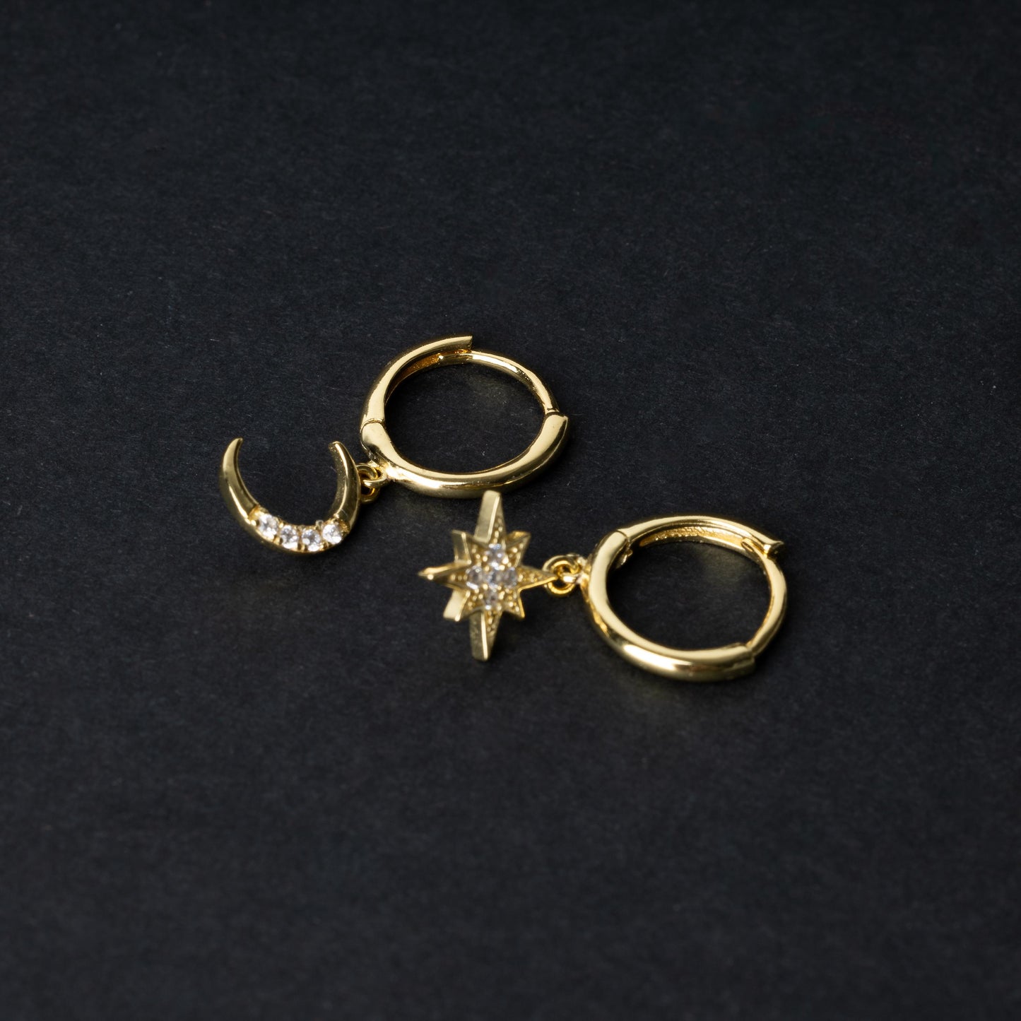 Gold moon and star hoop earrings with cubic zirconia accents, displayed on a dark background.