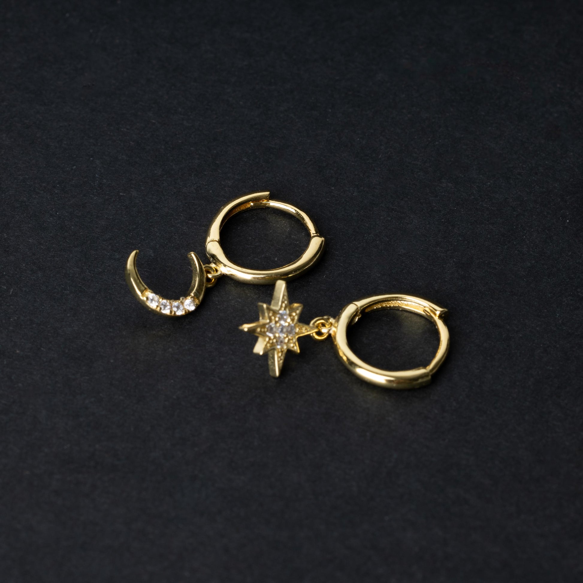 Gold moon and star hoop earrings with cubic zirconia accents, displayed on a dark background.