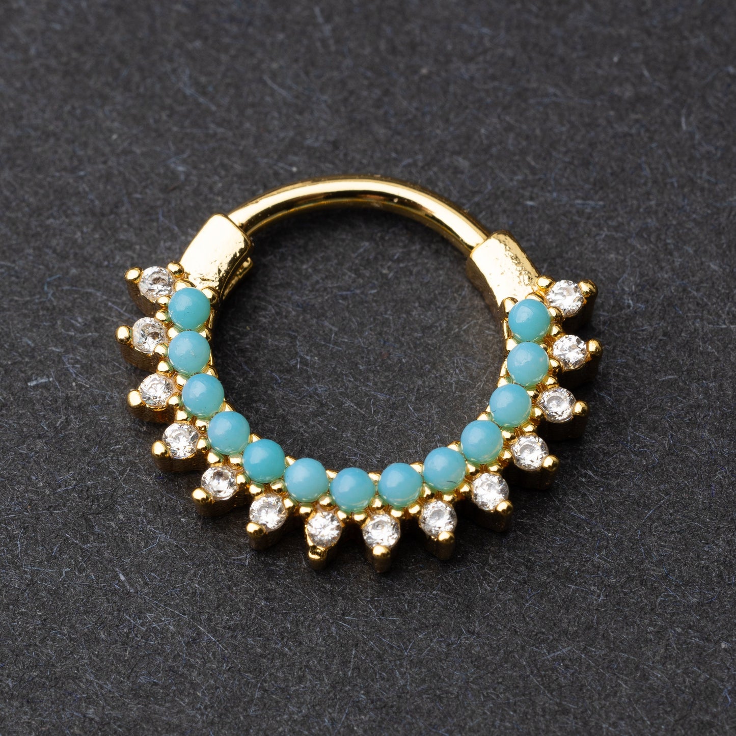 Gold-tone septum clicker with turquoise beads and cubic zirconia stones arranged in an elegant pattern, displayed on a dark background.