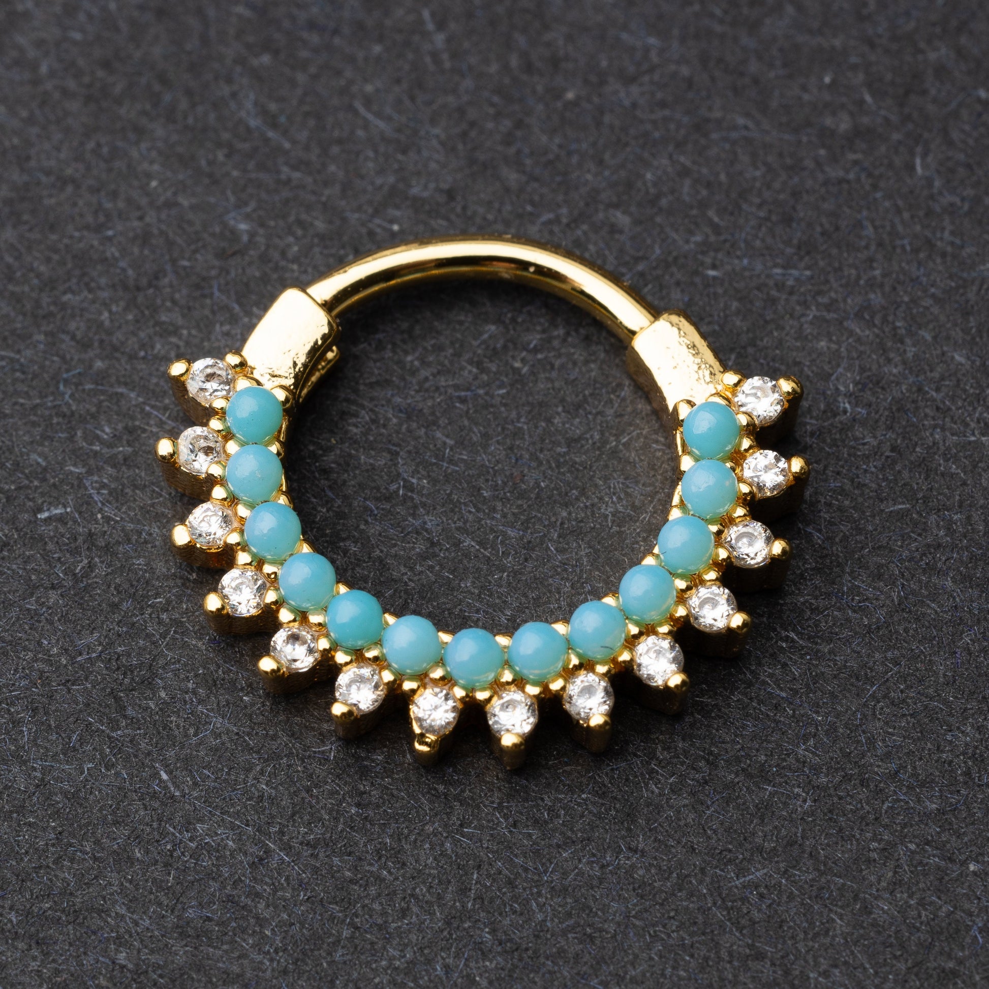Gold-tone septum clicker with turquoise beads and cubic zirconia stones arranged in an elegant pattern, displayed on a dark background.