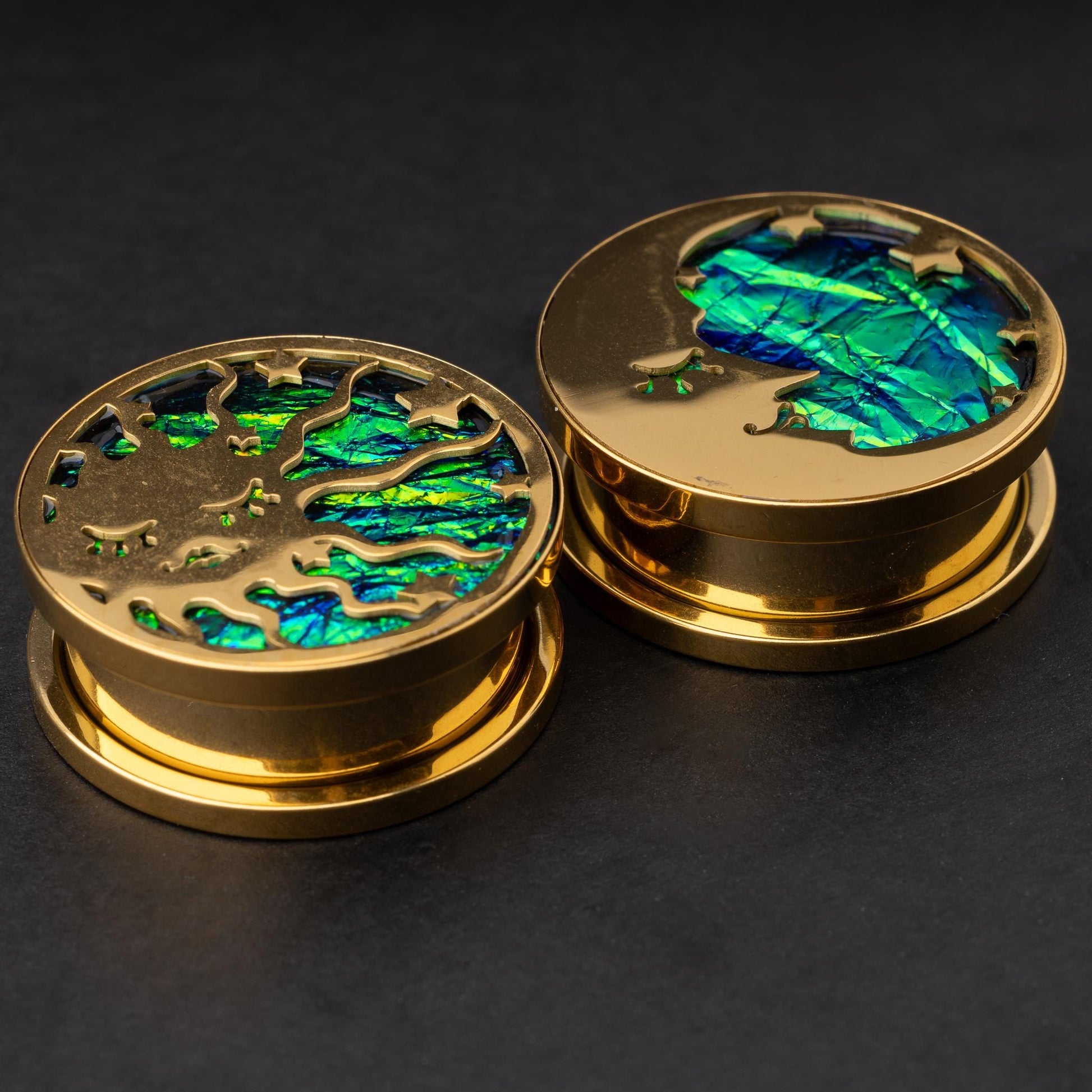 Gold plugs with sun and moon designs, accented by iridescent abalone inlay, displayed on a dark background.