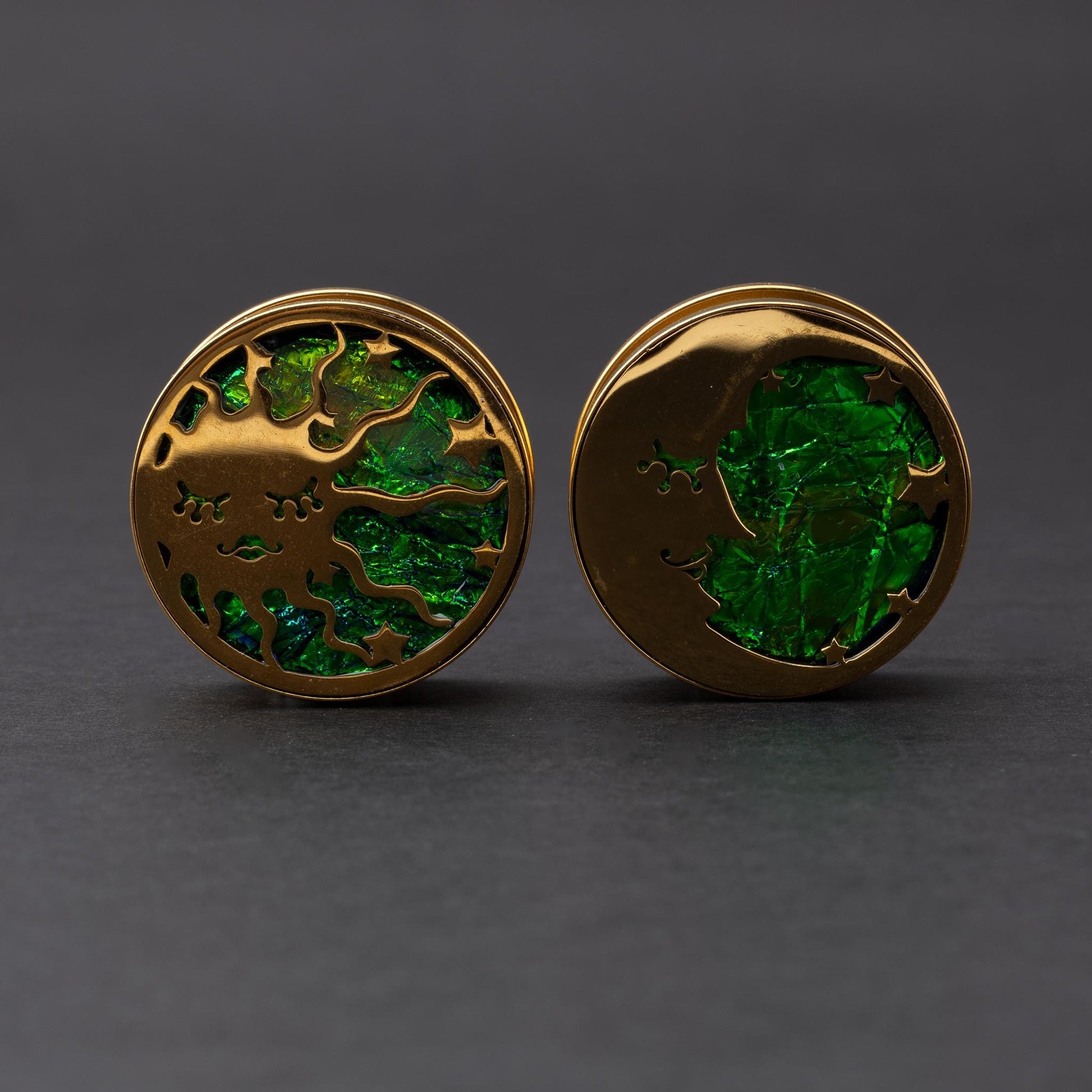 Gold plugs with sun and moon designs, accented by iridescent abalone inlay, displayed on a dark background.