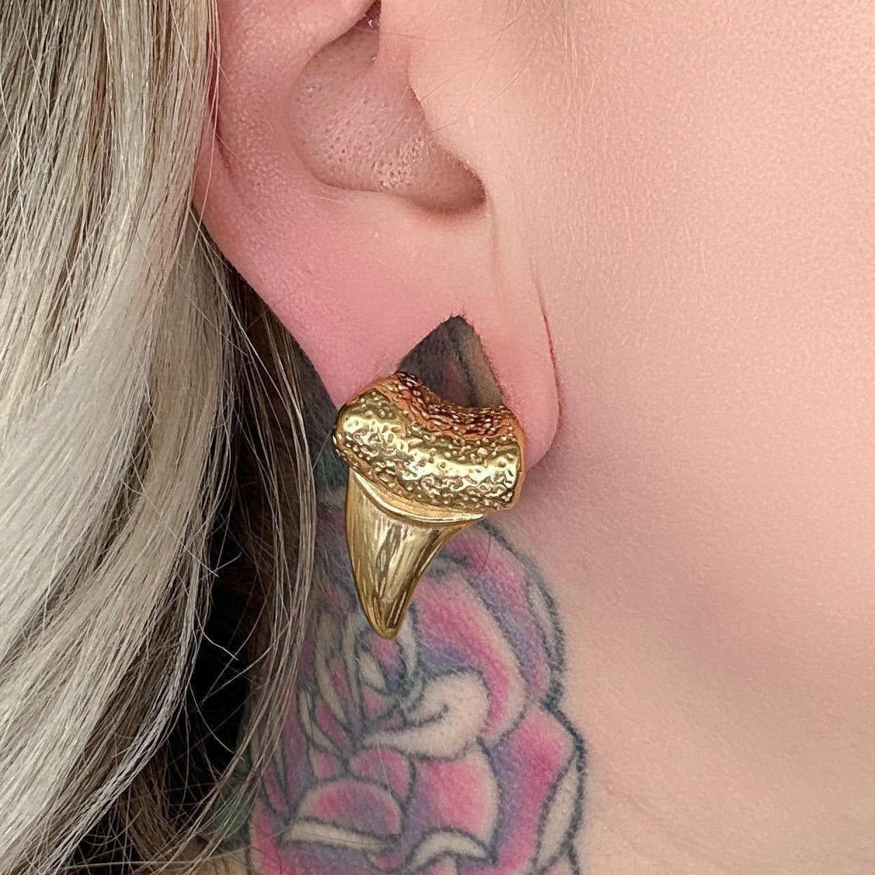Close-up of gold tooth ear weights on a female with a neck tattoo.

