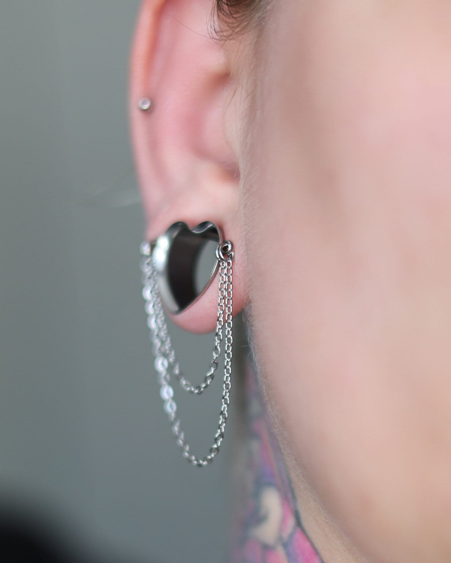 Heart-shaped tunnel with draped chains in silver, displayed in a models ear. 