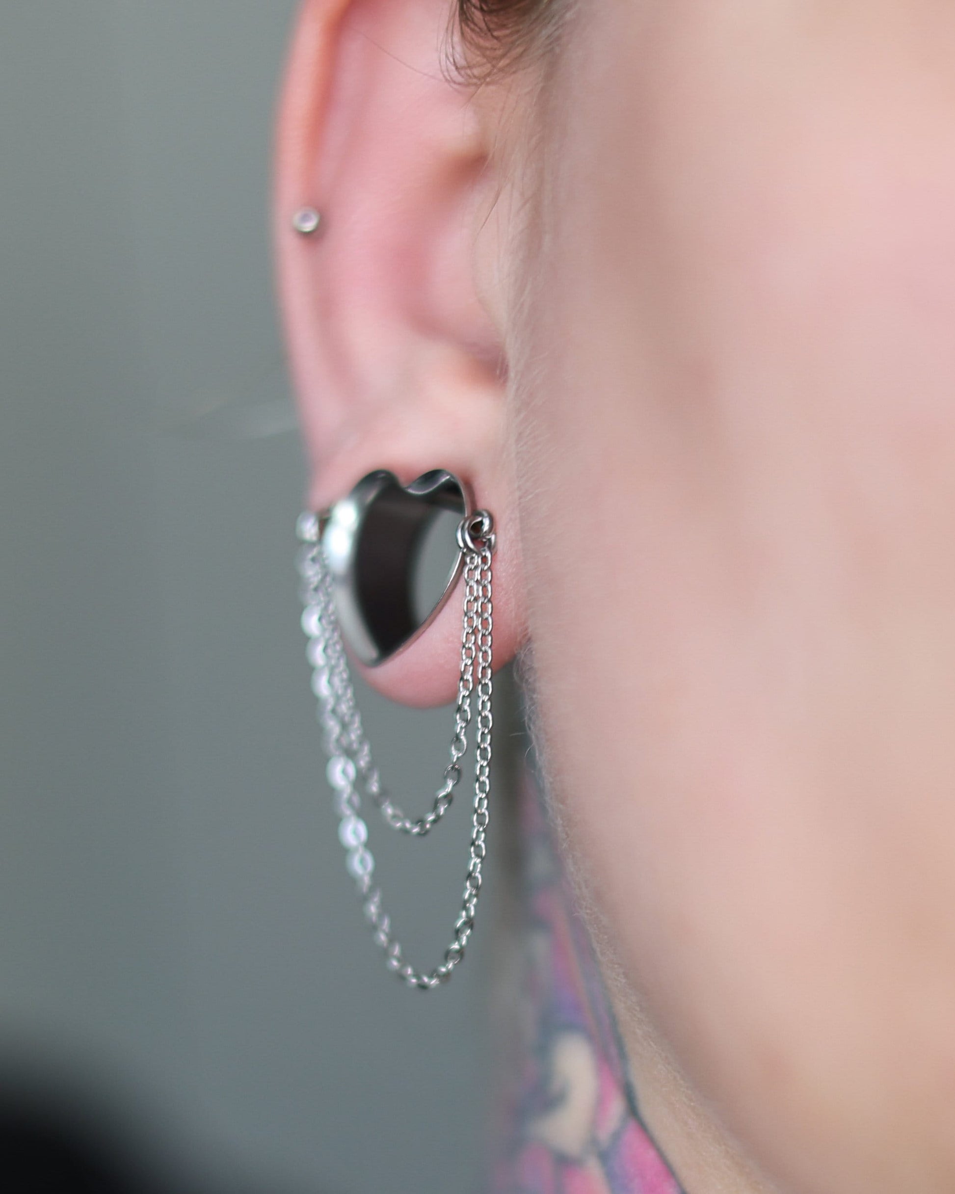 Heart-shaped tunnel with draped chains in silver, displayed in a models ear. 