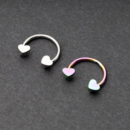 Two horseshoe-shaped hoops with heart-shaped ends in silver and rainbow finishes, displayed on a dark background.