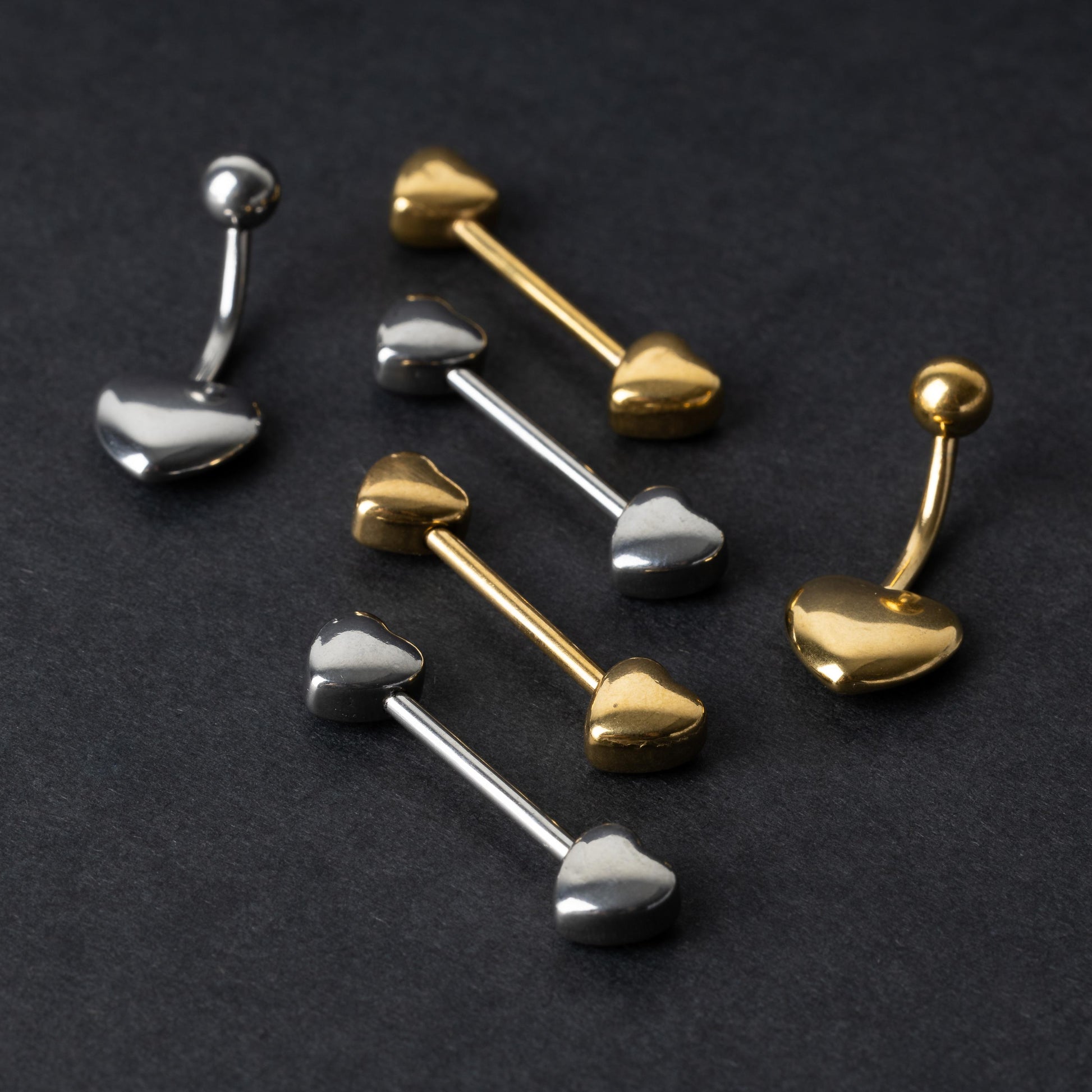 Heart-shaped silver and gold barbells and belly rings arranged on a dark background.