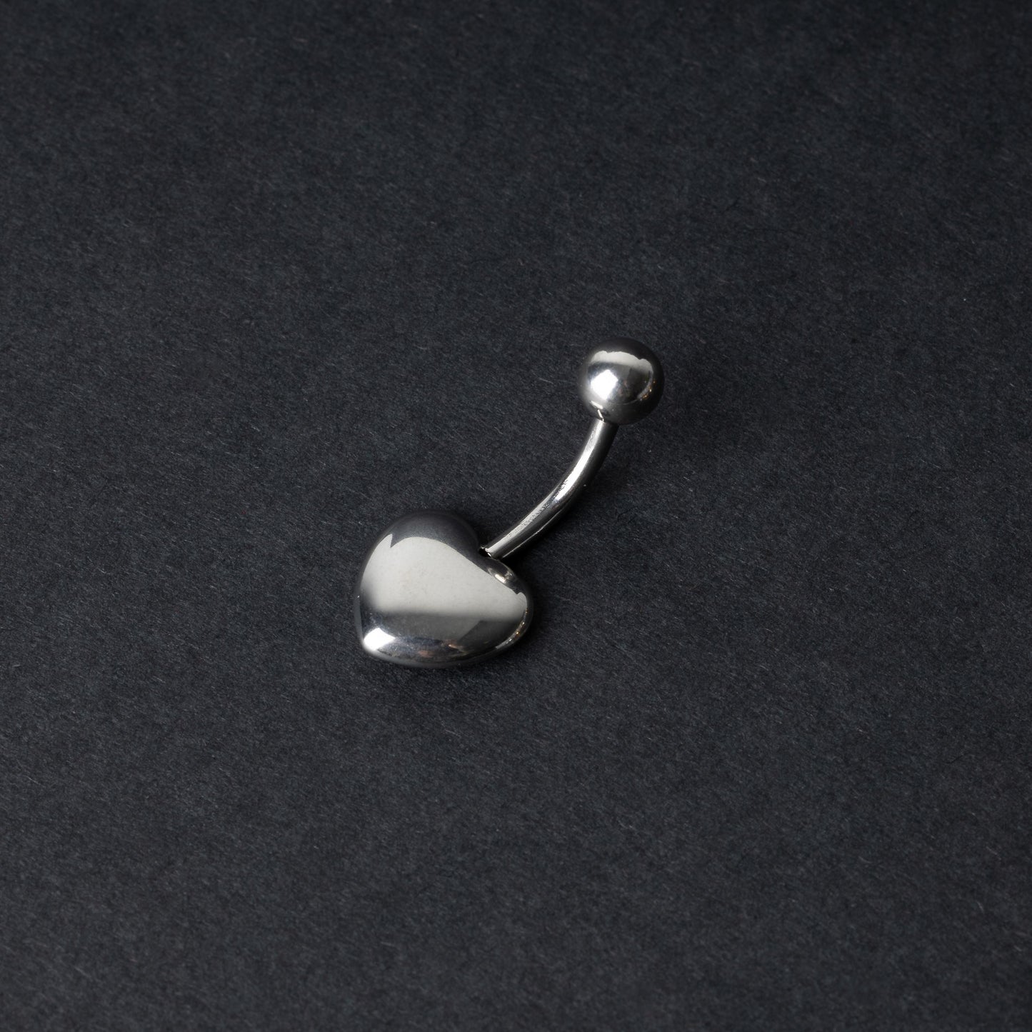 Silver heart shaped belly bar on a dark background