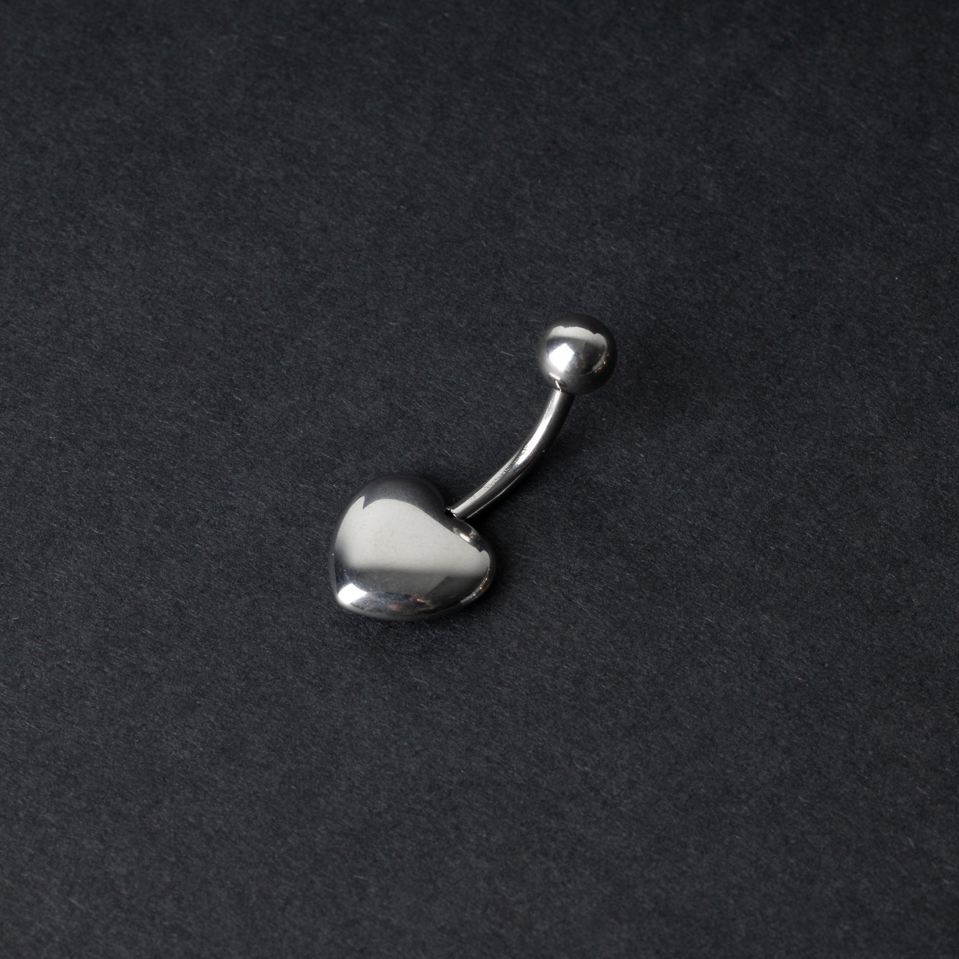 Silver heart shaped belly bar on a dark background