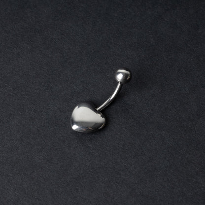 Silver heart shaped belly bar on a dark background