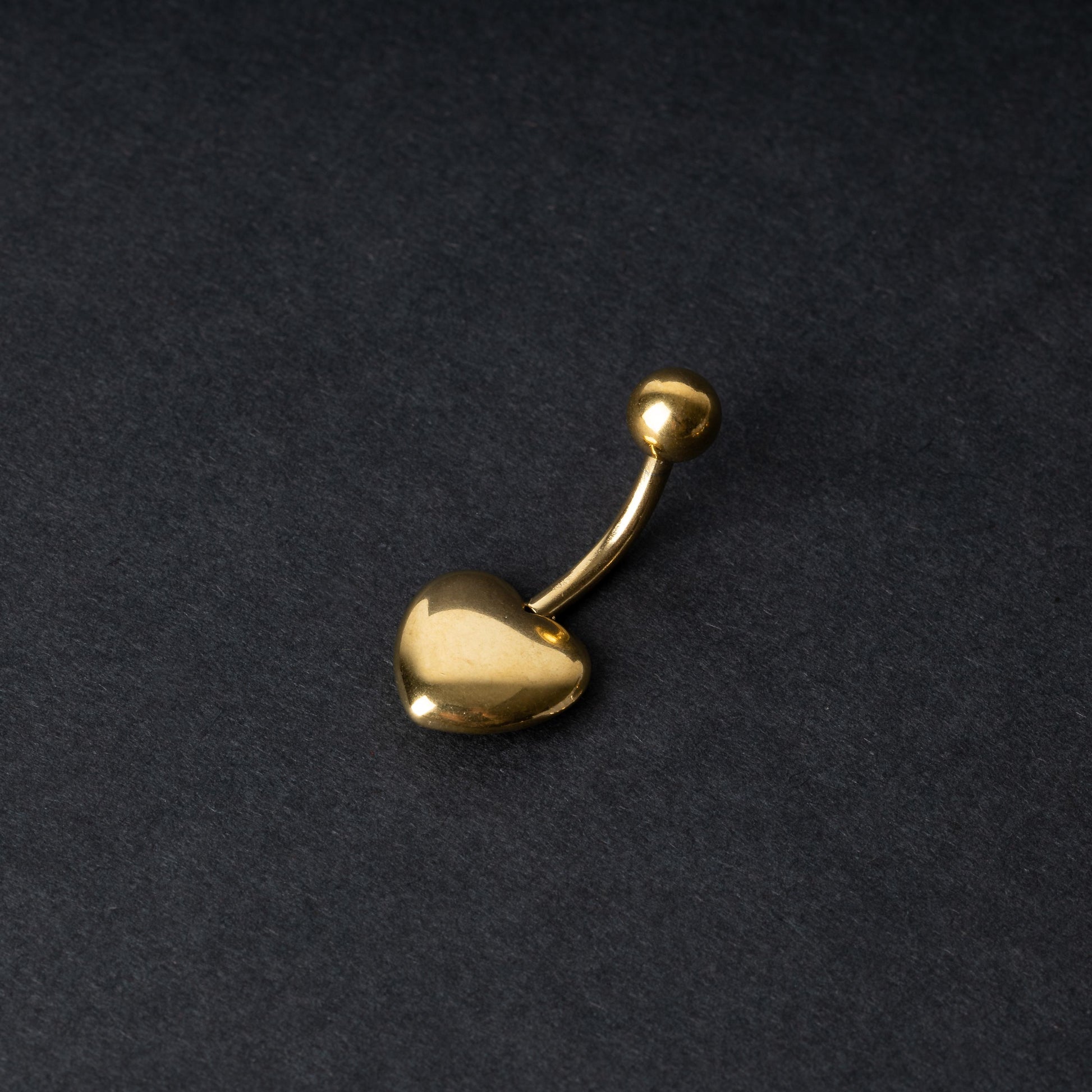 Gold heart shaped belly bar on a dark background