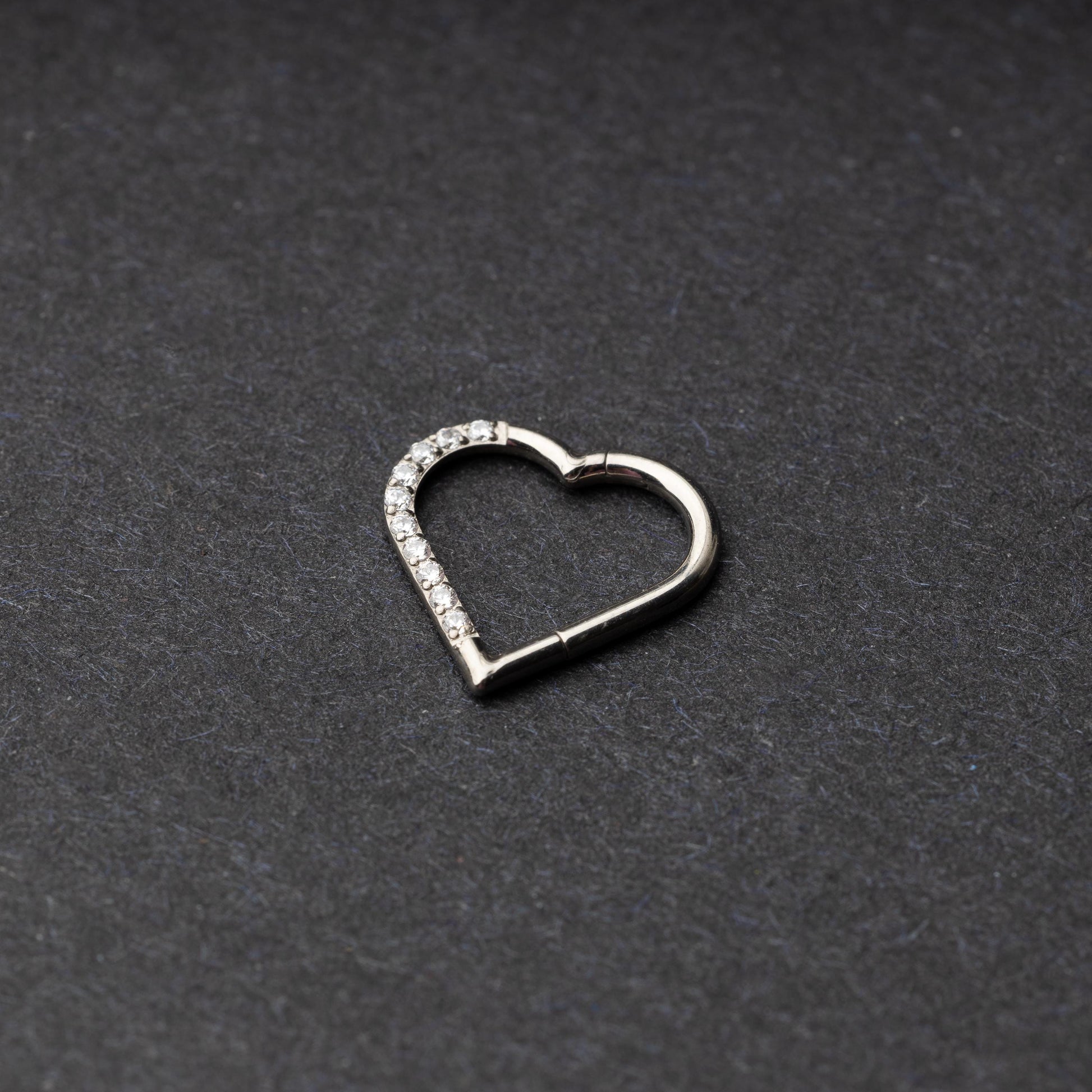 Heart-shaped daith clicker with crystal accents along one side, displayed on a dark textured background.