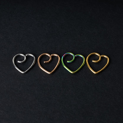 Four heart-shaped nose rings in silver, rose gold, rainbow, and gold finishes, displayed on a dark background.