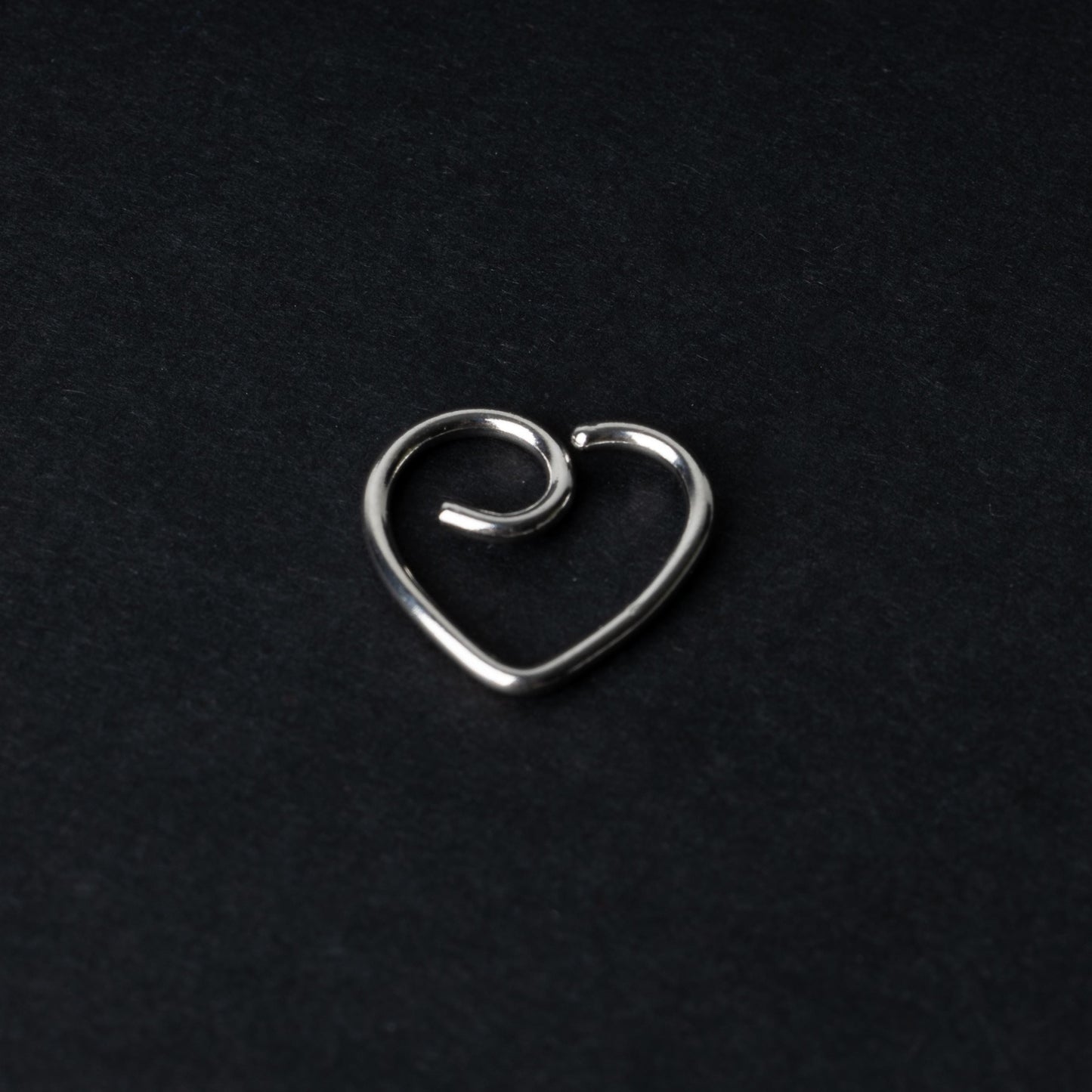 Silver heart shaped daith on a dark background